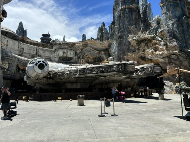 The Millennium Falcon spacecraft displayed in a rocky canyon setting with tall stone formations and park structures visible