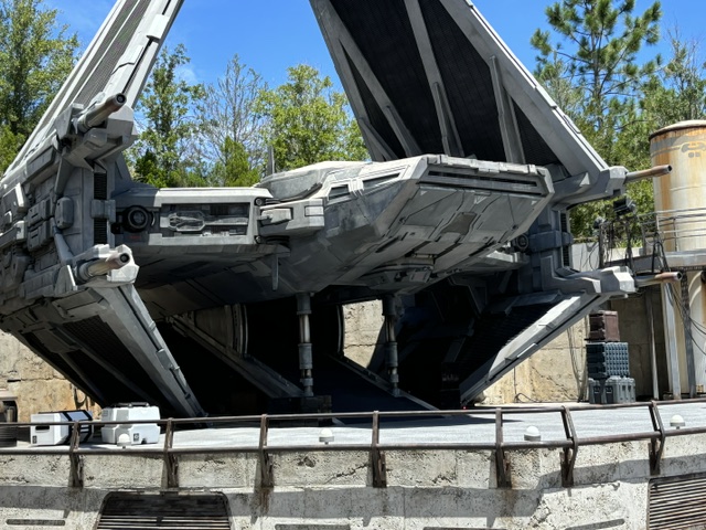 A large black spacecraft with open cargo bay doors displayed in an outdoor quarry-style setting with metal railings