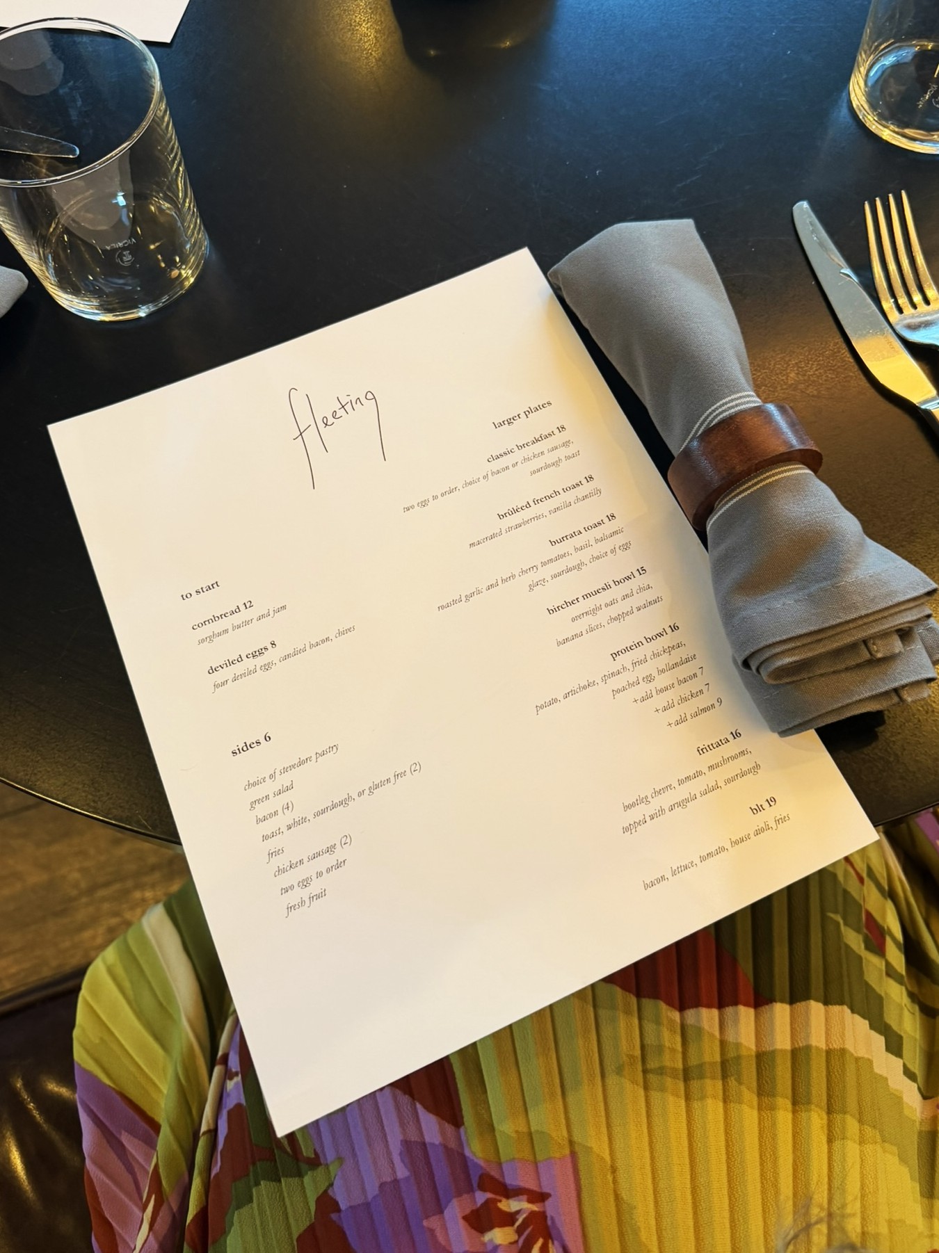 Restaurant menu titled 'Fleeting' displayed on black table with place setting and water glass