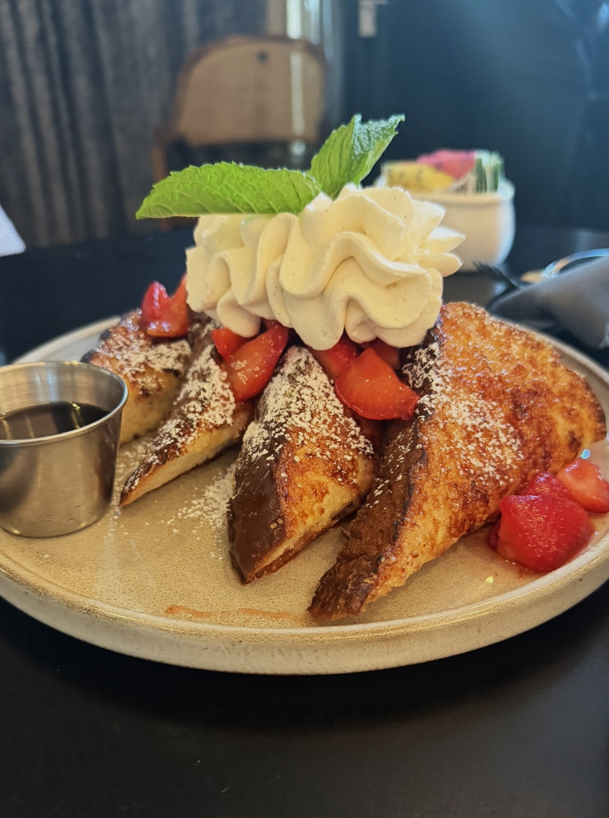 Plated French toast with whipped cream, fresh strawberries, and mint leaf garnish