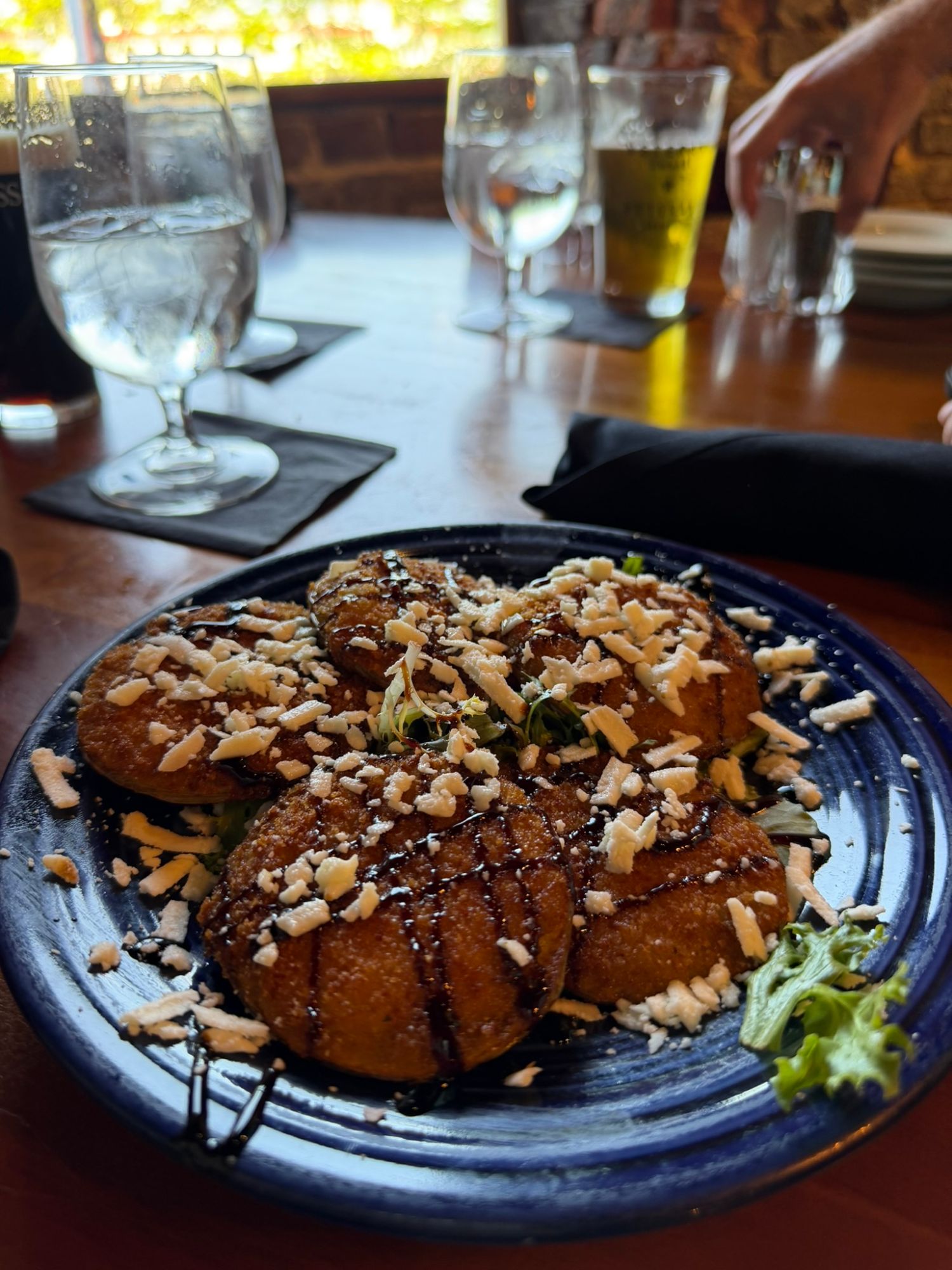 Almond-topped pastries on dark blue plate with water and beer glasses on wooden table