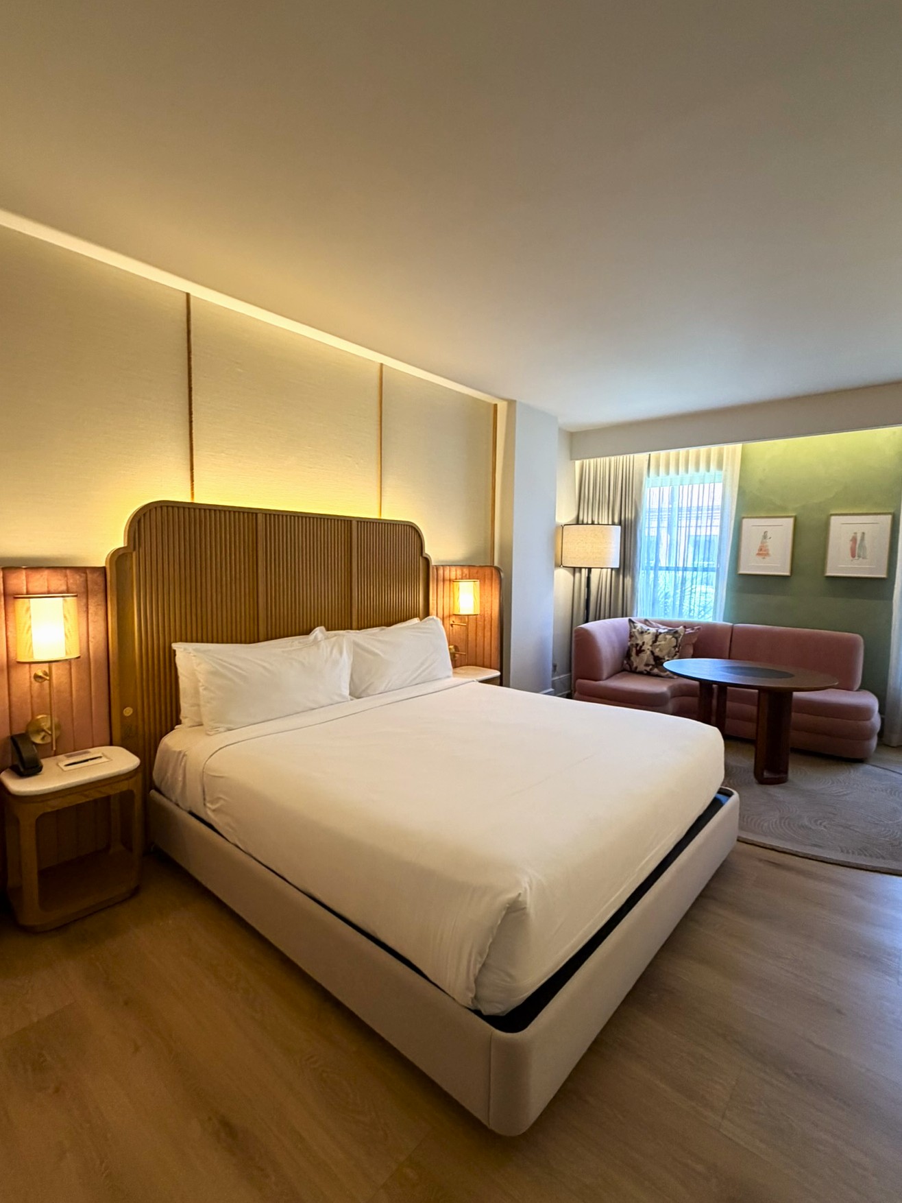 Elegant hotel bedroom with ribbed headboard, white bedding, and sitting area with green accent wall
