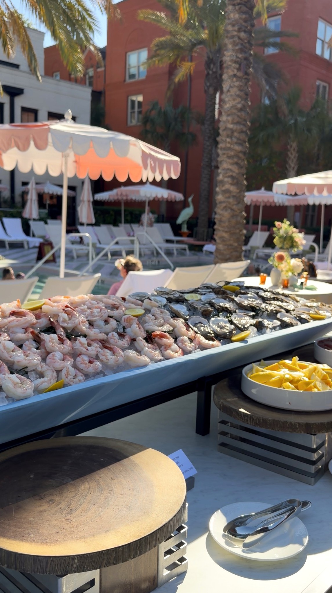 Outdoor seafood display with shrimp and oysters on ice, striped umbrellas, and palm trees