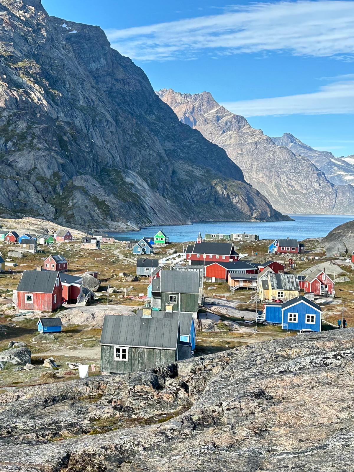 Aerial view of a Greenlandic village with red, blue, and yellow houses nestled between rocky terrain and a fjord