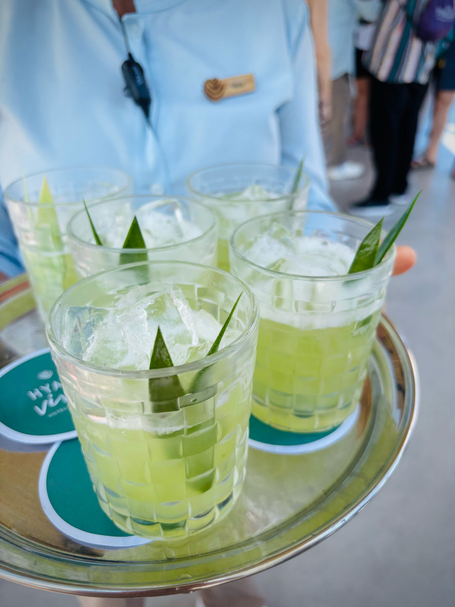 Server in light blue uniform holding tray with three lime-garnished cocktails at a Riviera Maya resort