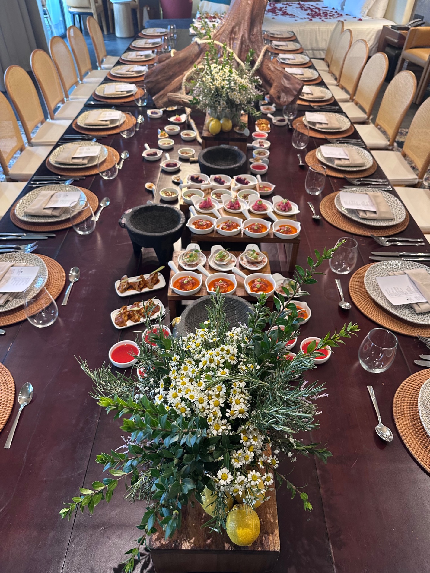Long dining table set for formal dinner with floral centerpiece, place settings, and appetizers under dramatic wooden beams