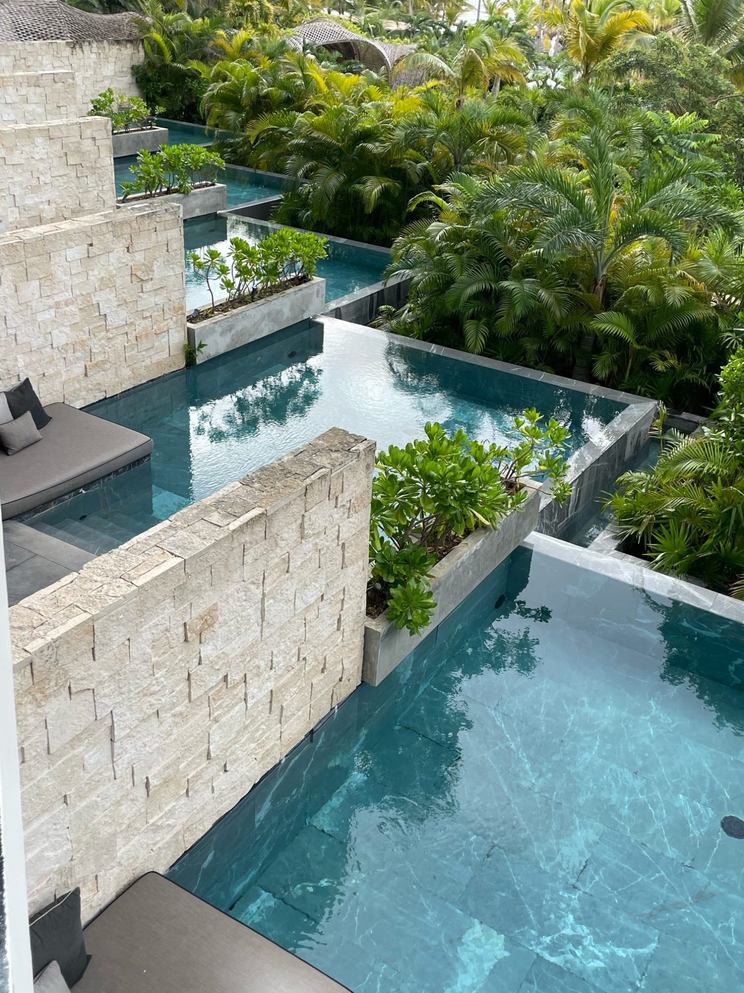 Cascading pools connected by stone walls surrounded by lush tropical vegetation and palm trees at a resort