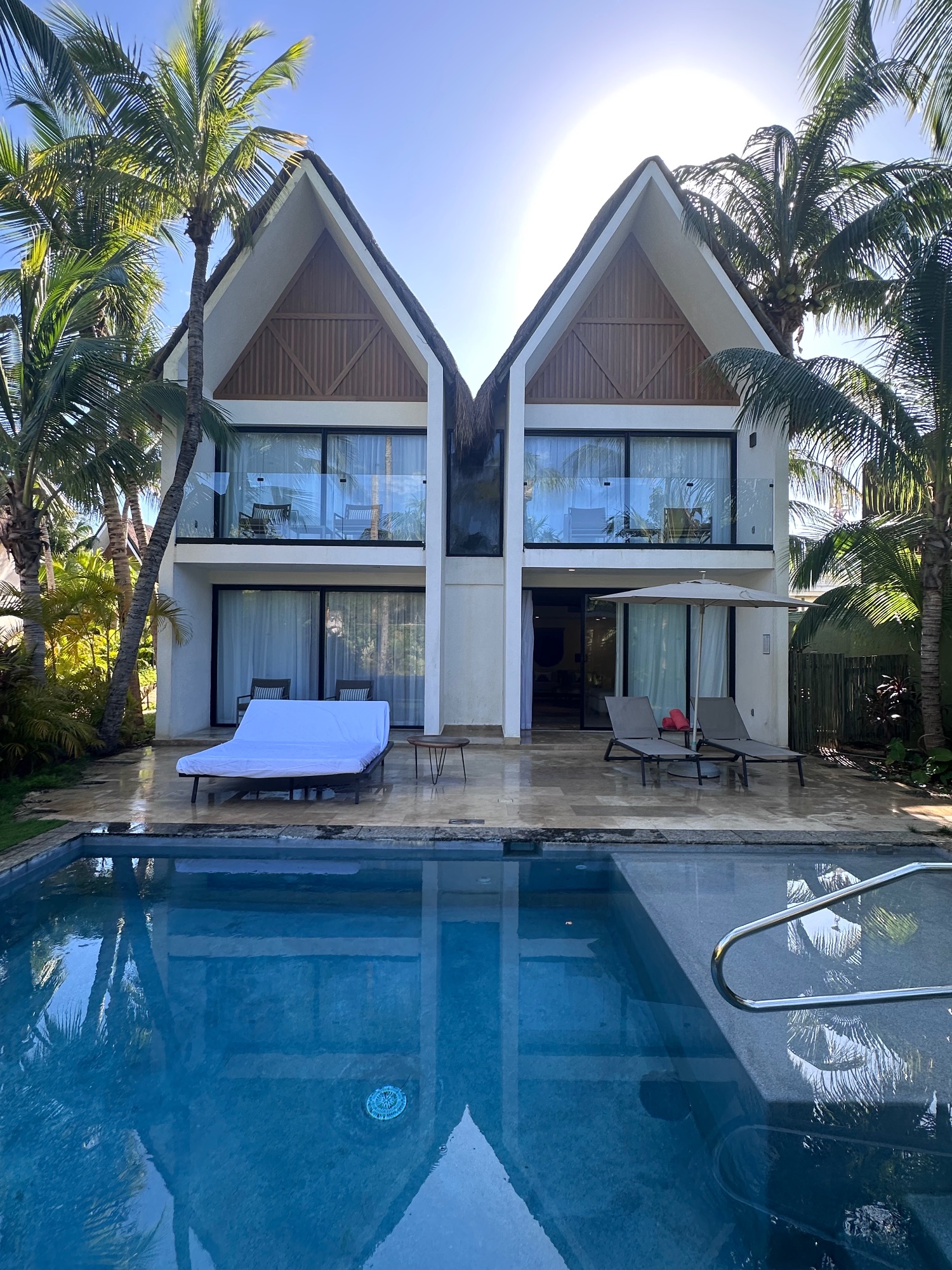 Modern white villa with peaked roof design, pool in foreground, palm trees, and tropical landscaping