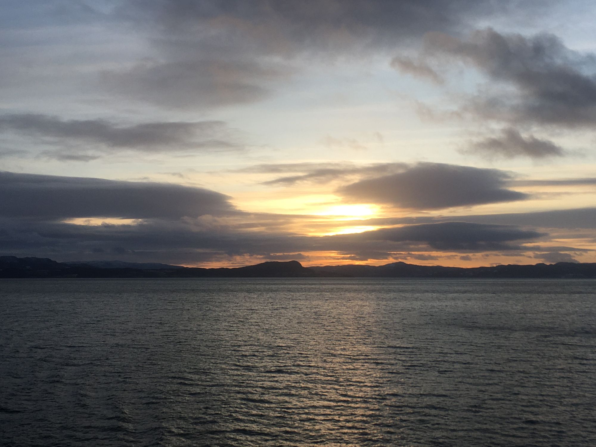 Golden sunset over calm sea with dark mountain silhouettes on horizon