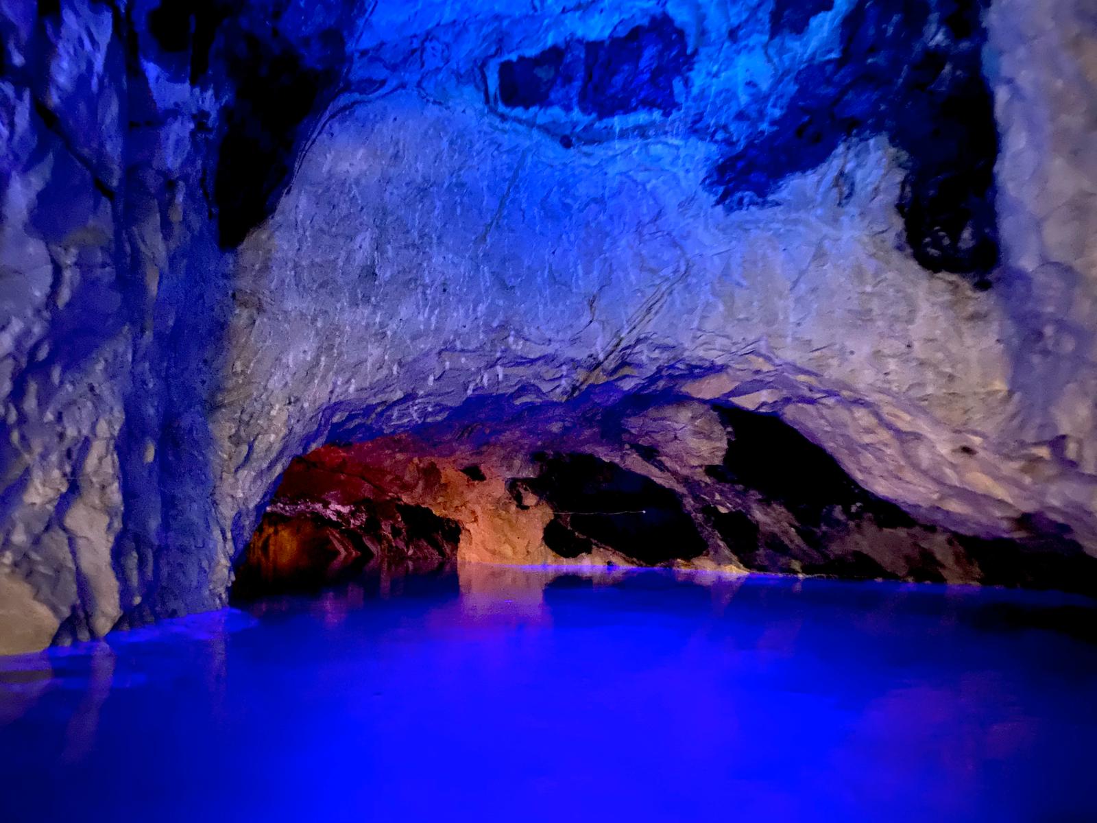 Blue-lit ice cave interior with white and purple-tinted frozen walls and reflective water below