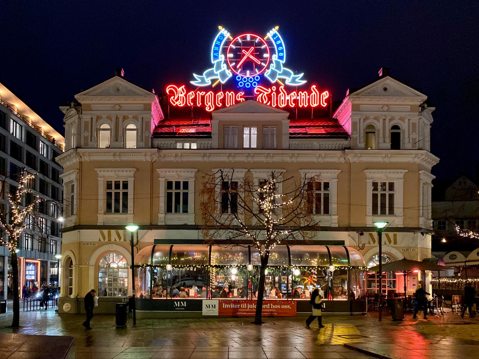 Bergens Zidende neon sign glowing red and blue above historic cream-colored building at night