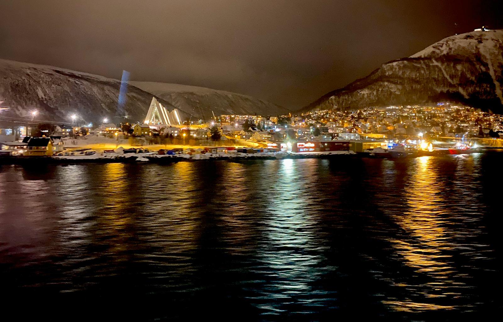 Snowy Arctic town with illuminated church and buildings nestled between snow-covered mountains at night