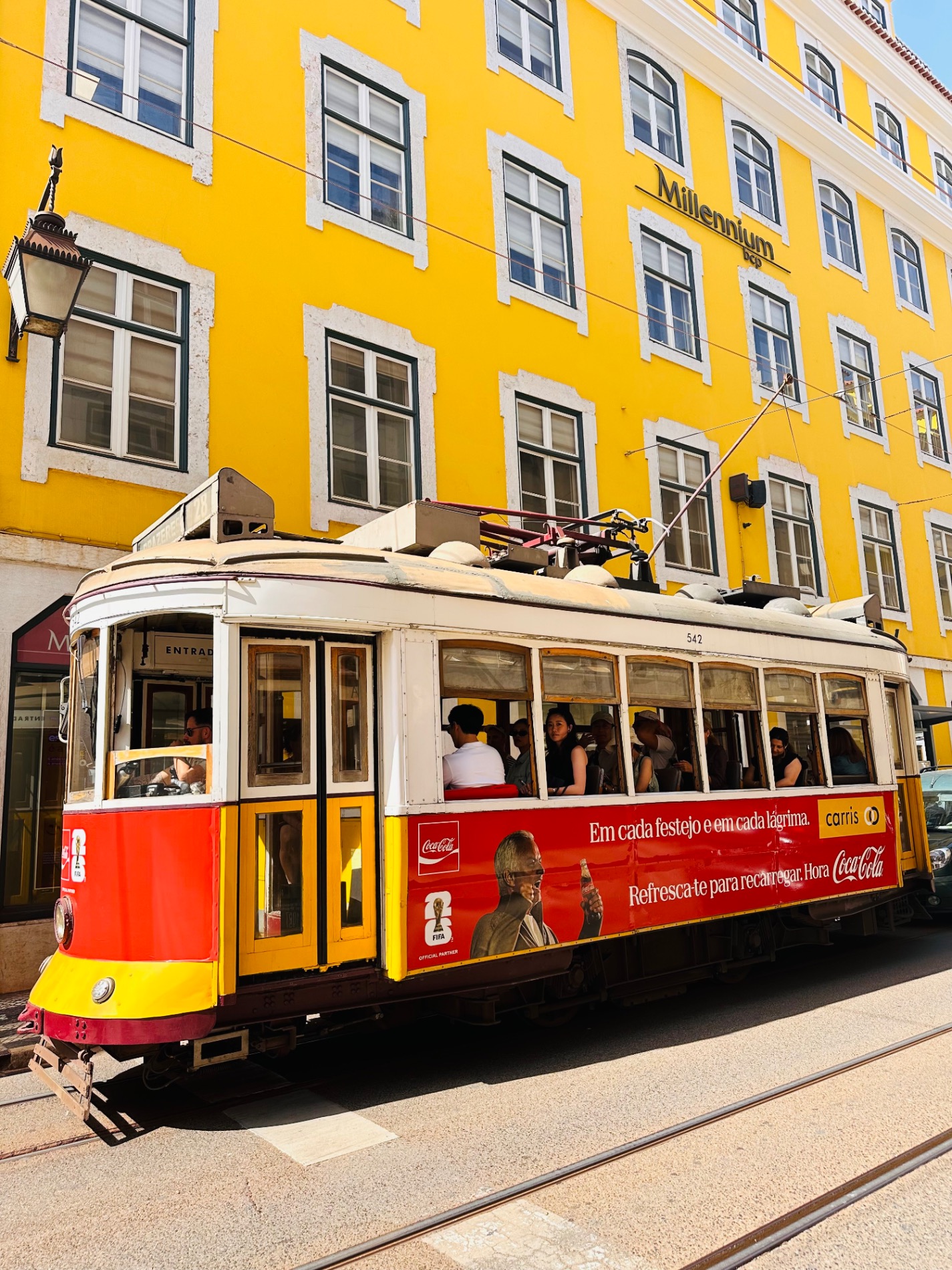 Red and yellow vintage tram number 542 passes a bright yellow building on a Lisbon street