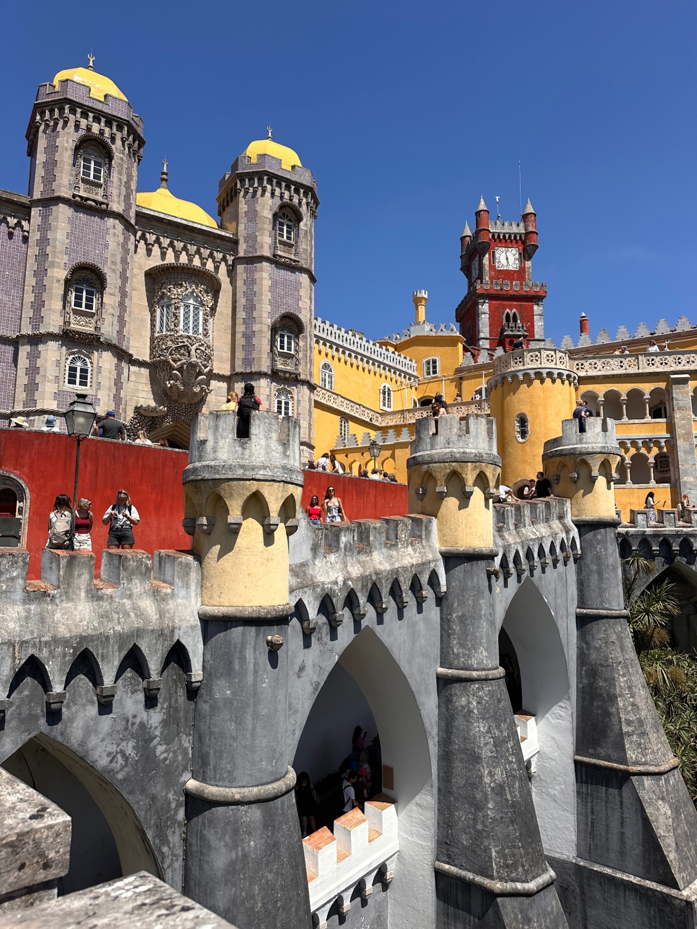 Colorful palace with yellow domes, red tower, and white stone bridge spanning a courtyard in Sintra