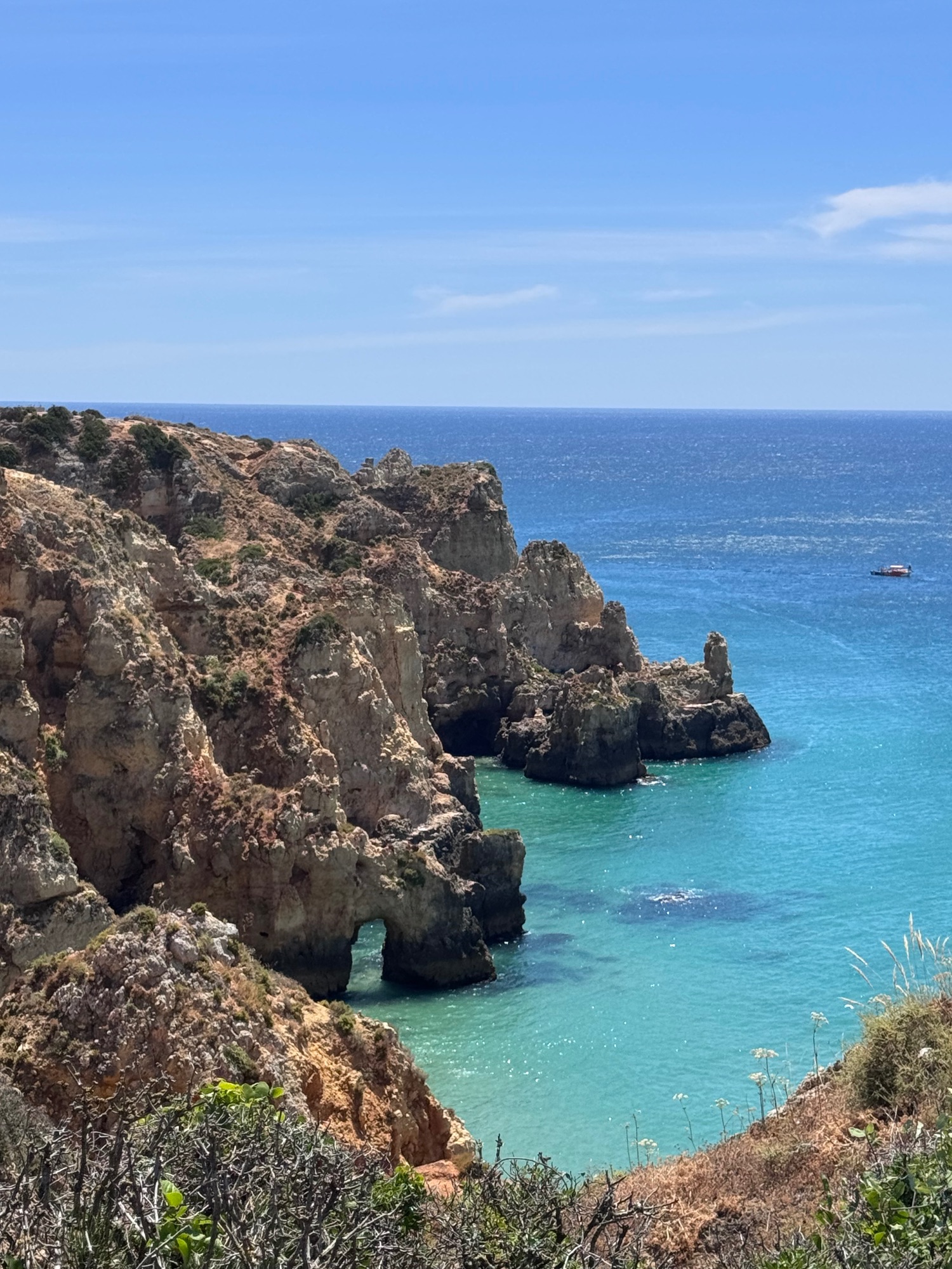 Man pushes stroller past rocky cliffs and Mediterranean beach with sparse vegetation