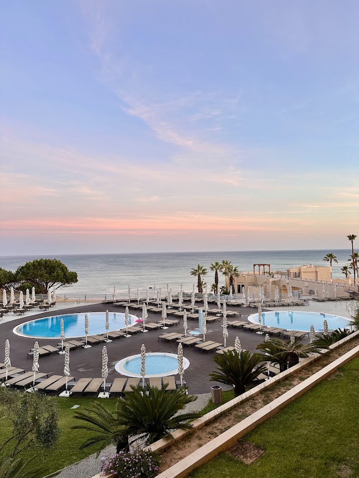 Beachfront resort pools and loungers at sunset with palm trees and calm sea beyond