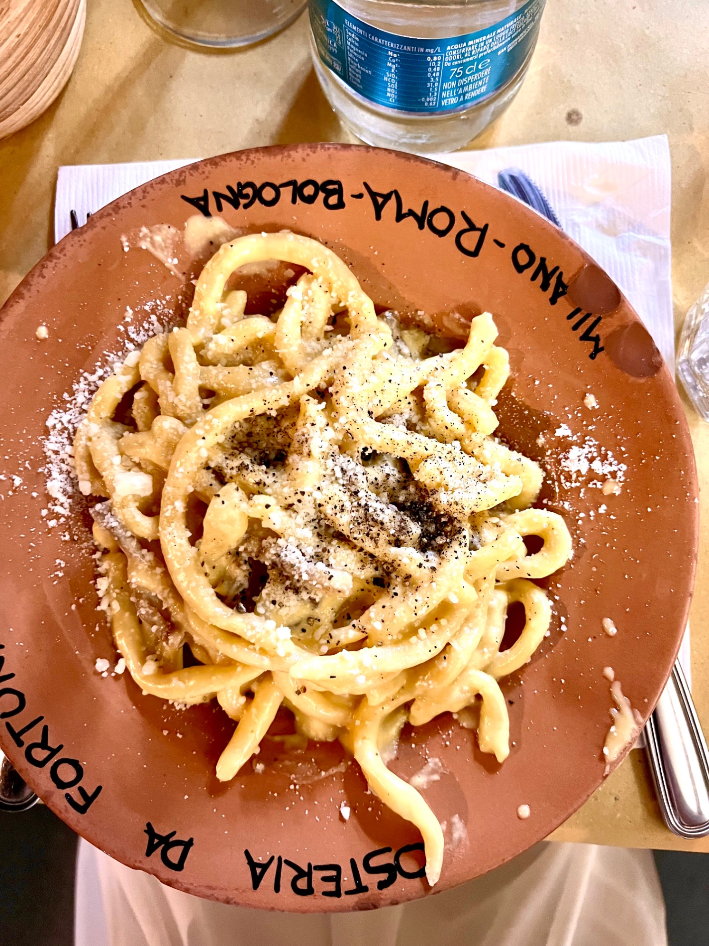 Plate of cacio e pepe pasta topped with black pepper and cheese on a terracotta dish at a restaurant on the Amalfi Coast