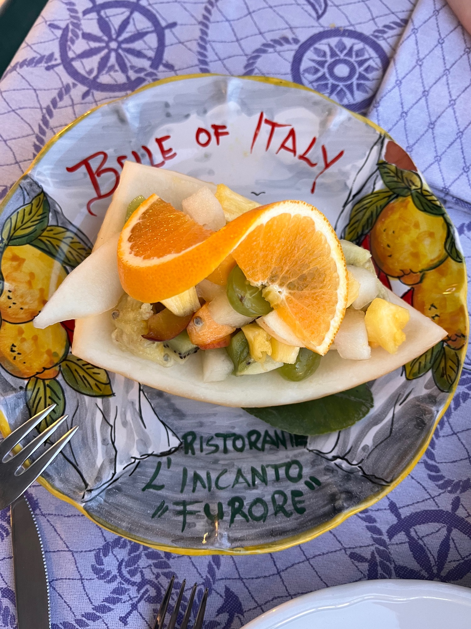 Fresh seafood dish with white fish, orange slices, and capers on a decorative plate labeled 'Brivle of Italy' at a coastal restaurant