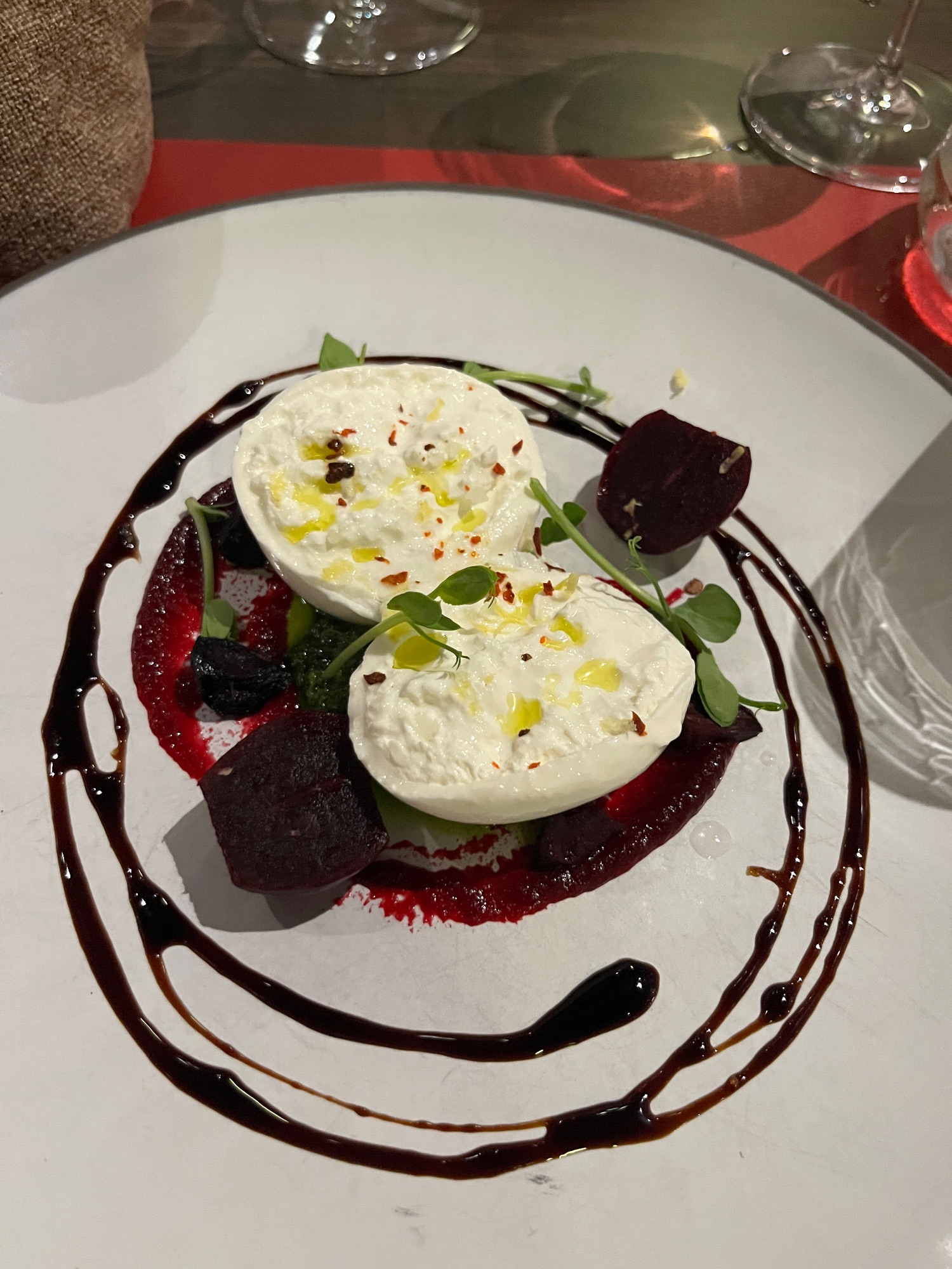 Artfully plated appetizer with burrata cheese, beets, and microgreens drizzled with dark reduction on a white plate