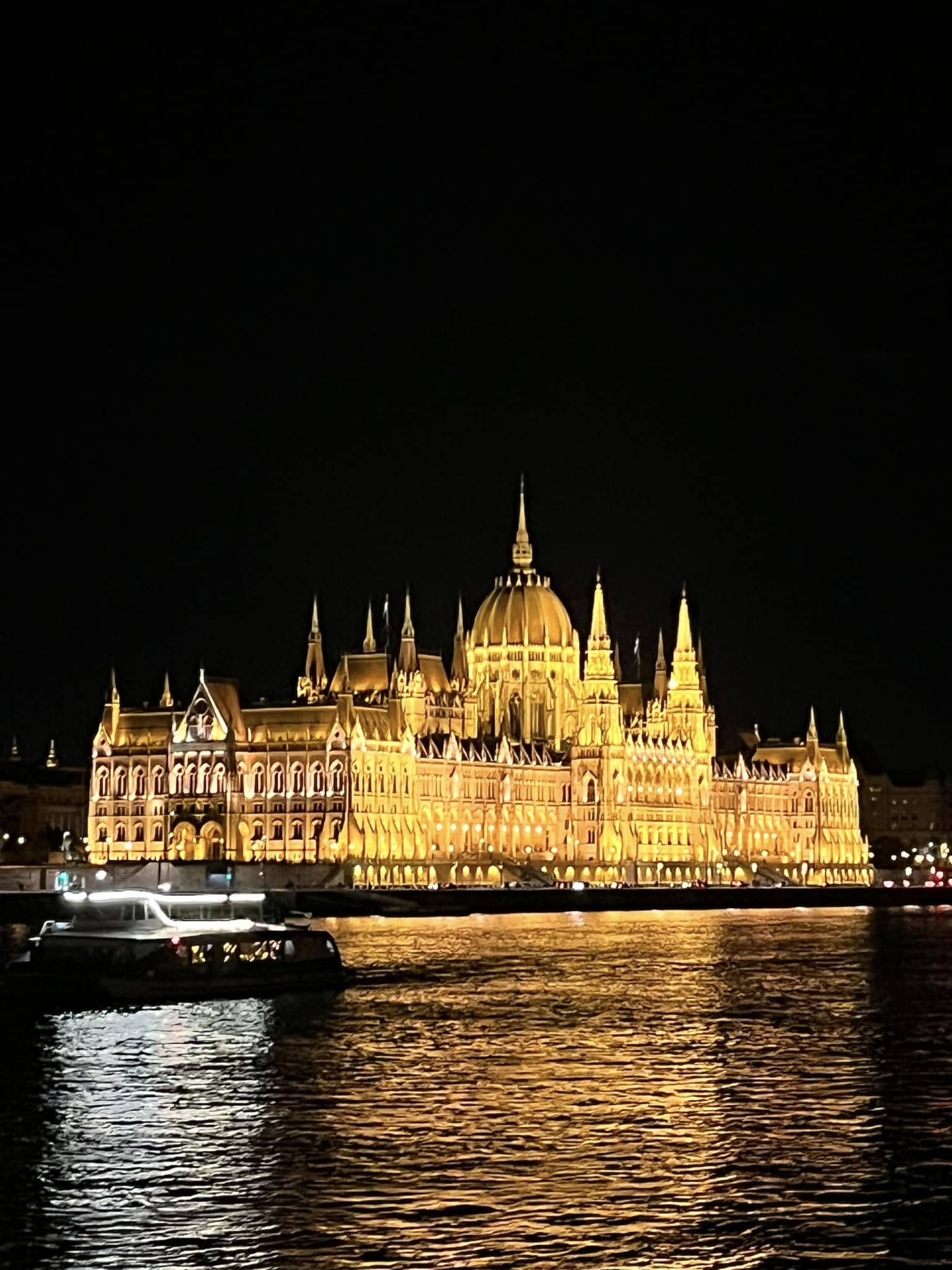 Hungarian Parliament Building illuminated at night across the Danube River with a tour boat in the foreground