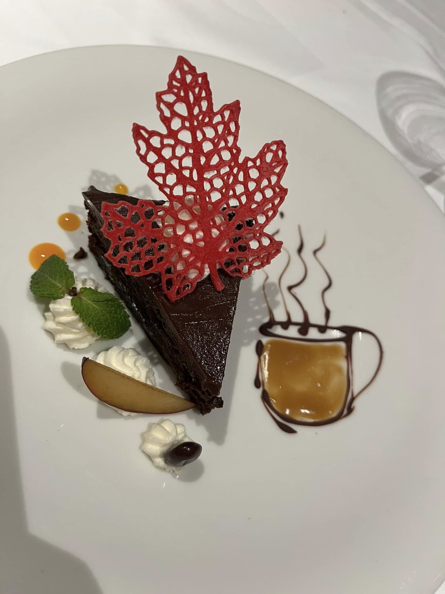Elegantly plated chocolate dessert with red lace leaf decoration, whipped cream, and caramel sauce on white plate