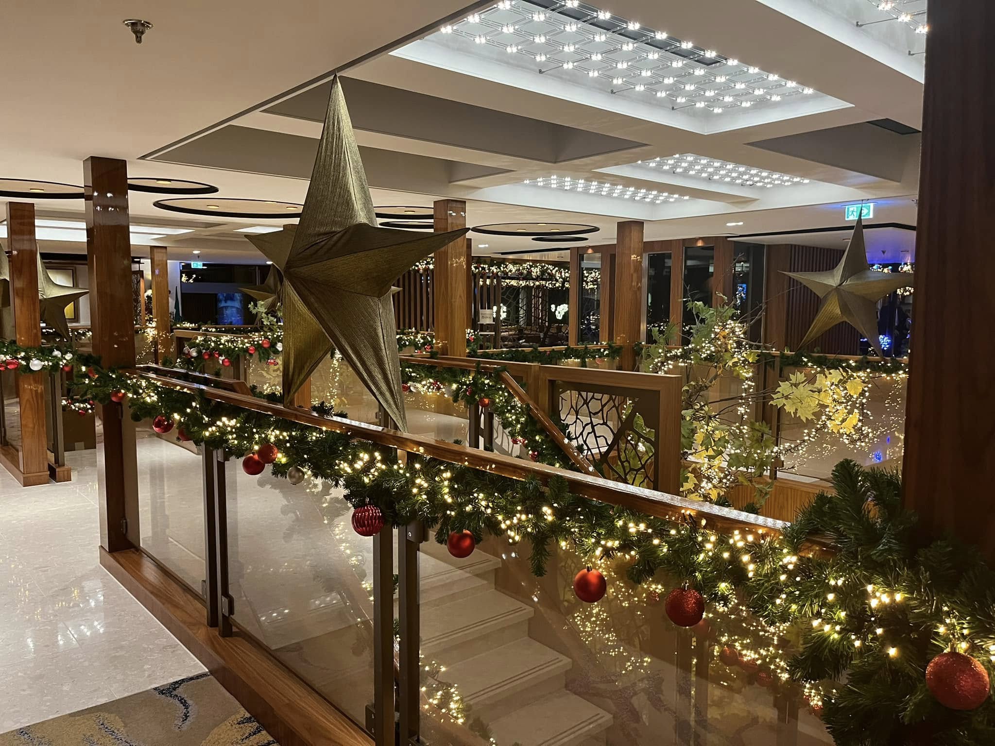 Cruise ship interior decorated for Christmas with garland, large gold stars, red and gold ornaments, and twinkling lights