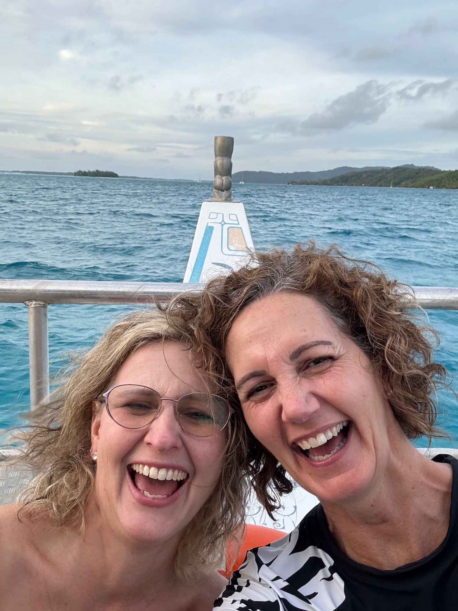 Two women with curly hair smiling at camera on boat with ocean and islands in background