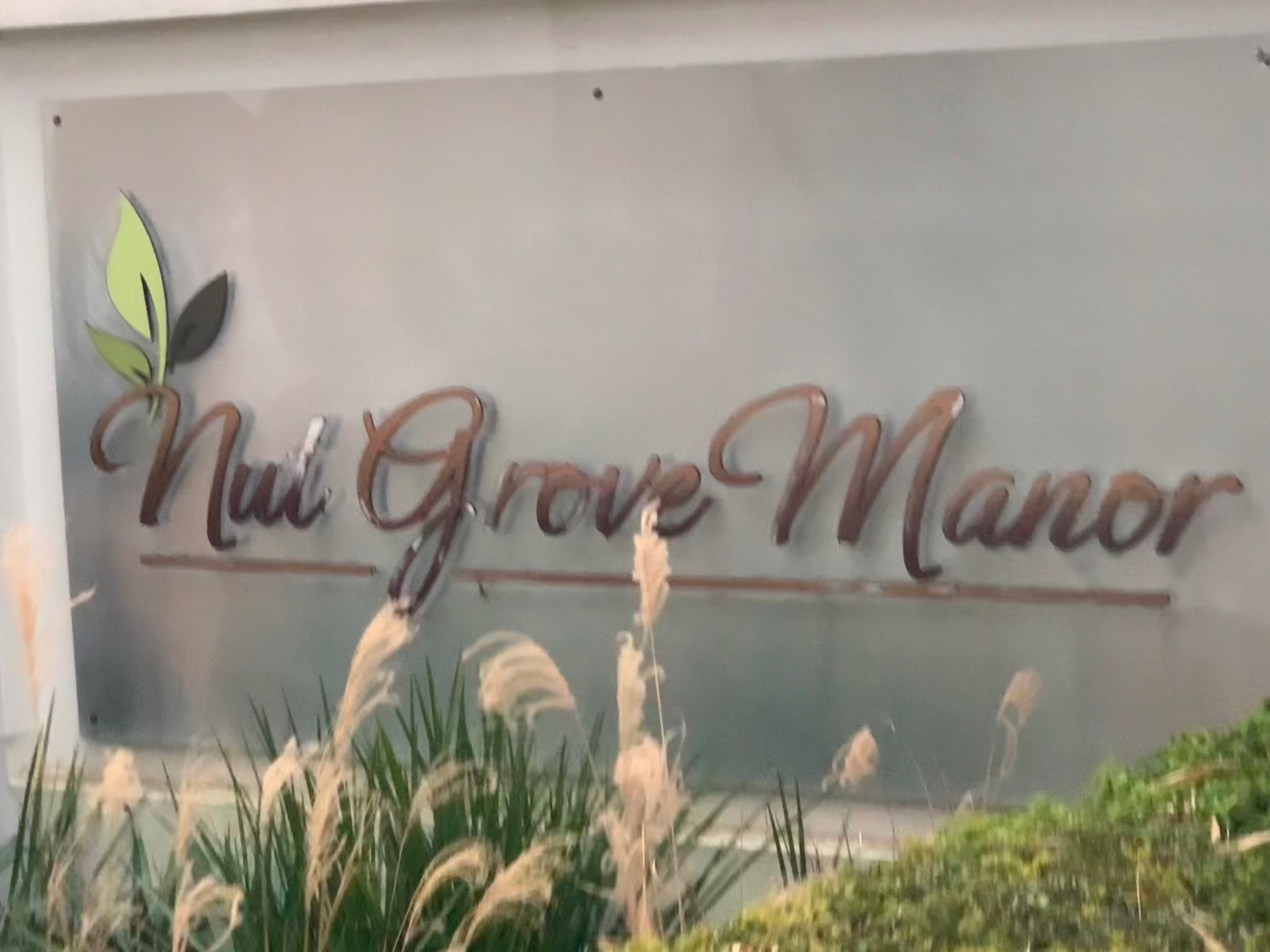 Nul Grove Manor sign with decorative grasses and foliage in soft focus