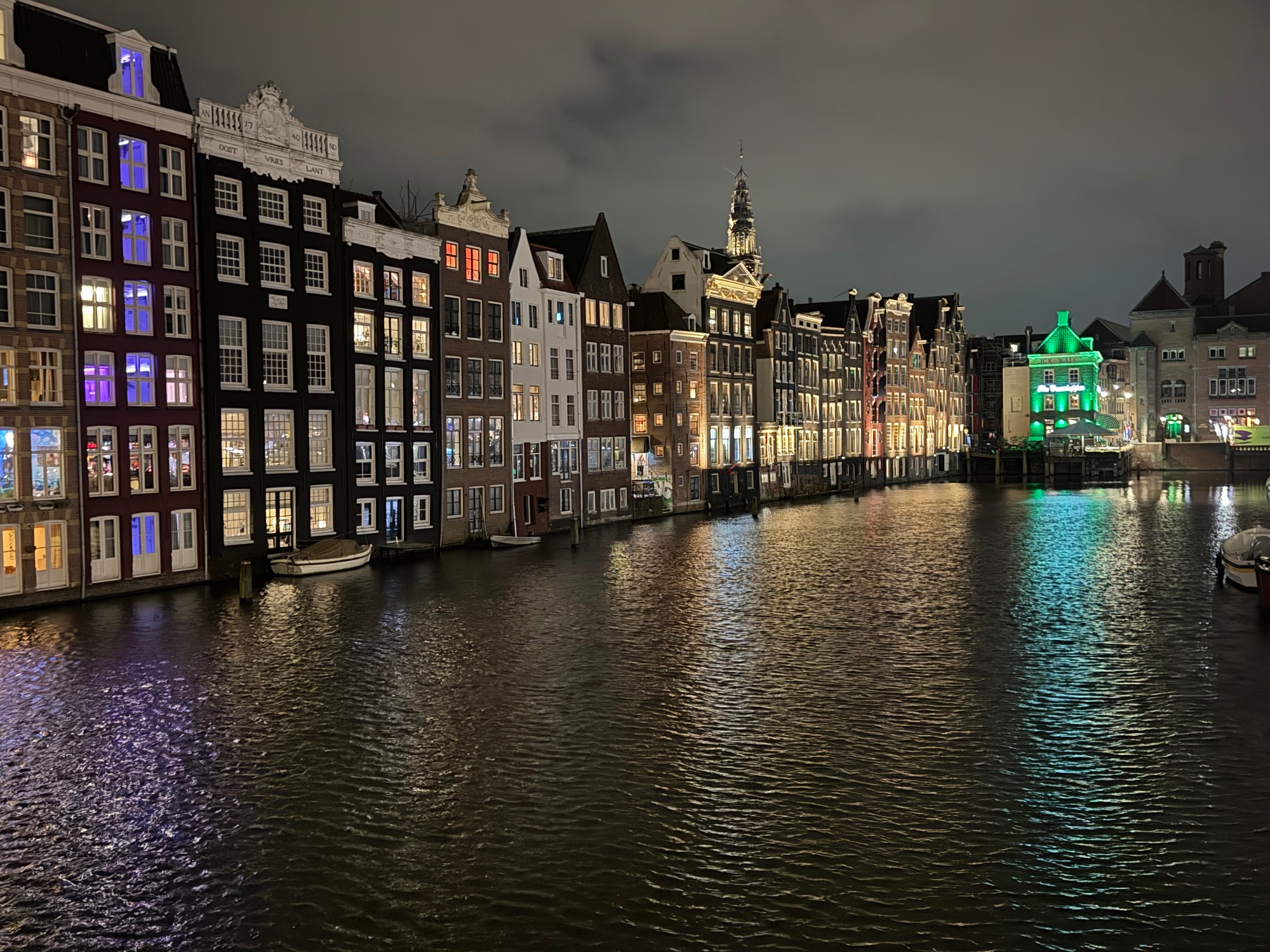 Illuminated canal-side buildings in Amsterdam at night, with colorful reflections on the water and traditional Dutch architecture