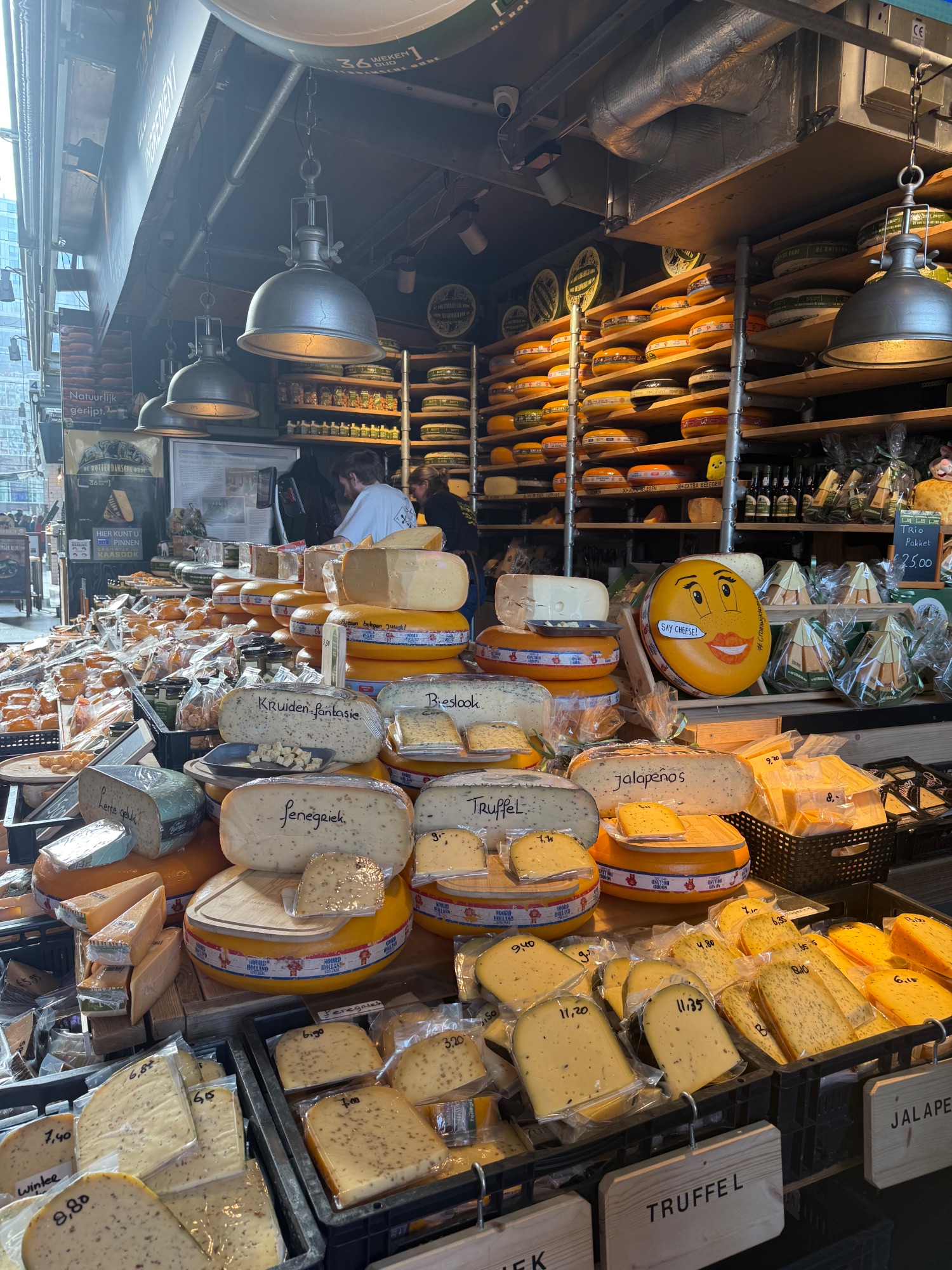 Cheese shop storefront in Amsterdam displaying wheels of yellow and white Dutch cheese with price labels