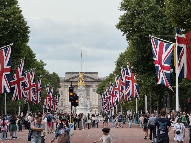 Union Jack flags line The Mall leading to Buckingham Palace with crowds of visitors on a cloudy afternoon