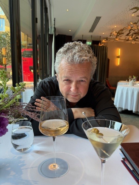 A man in dark clothing enjoys a glass of white wine at an upscale restaurant with modern interior design