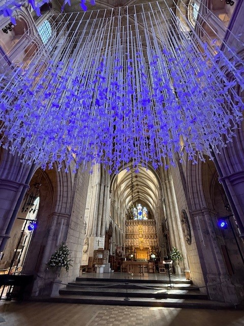 Purple-lit crystal chandelier installation hanging from the vaulted ceiling of a Gothic cathedral interior