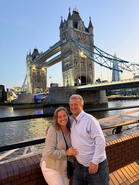 Mary Pat Sullivan and a companion stand together at Tower Bridge with the Thames and bridge structure behind them