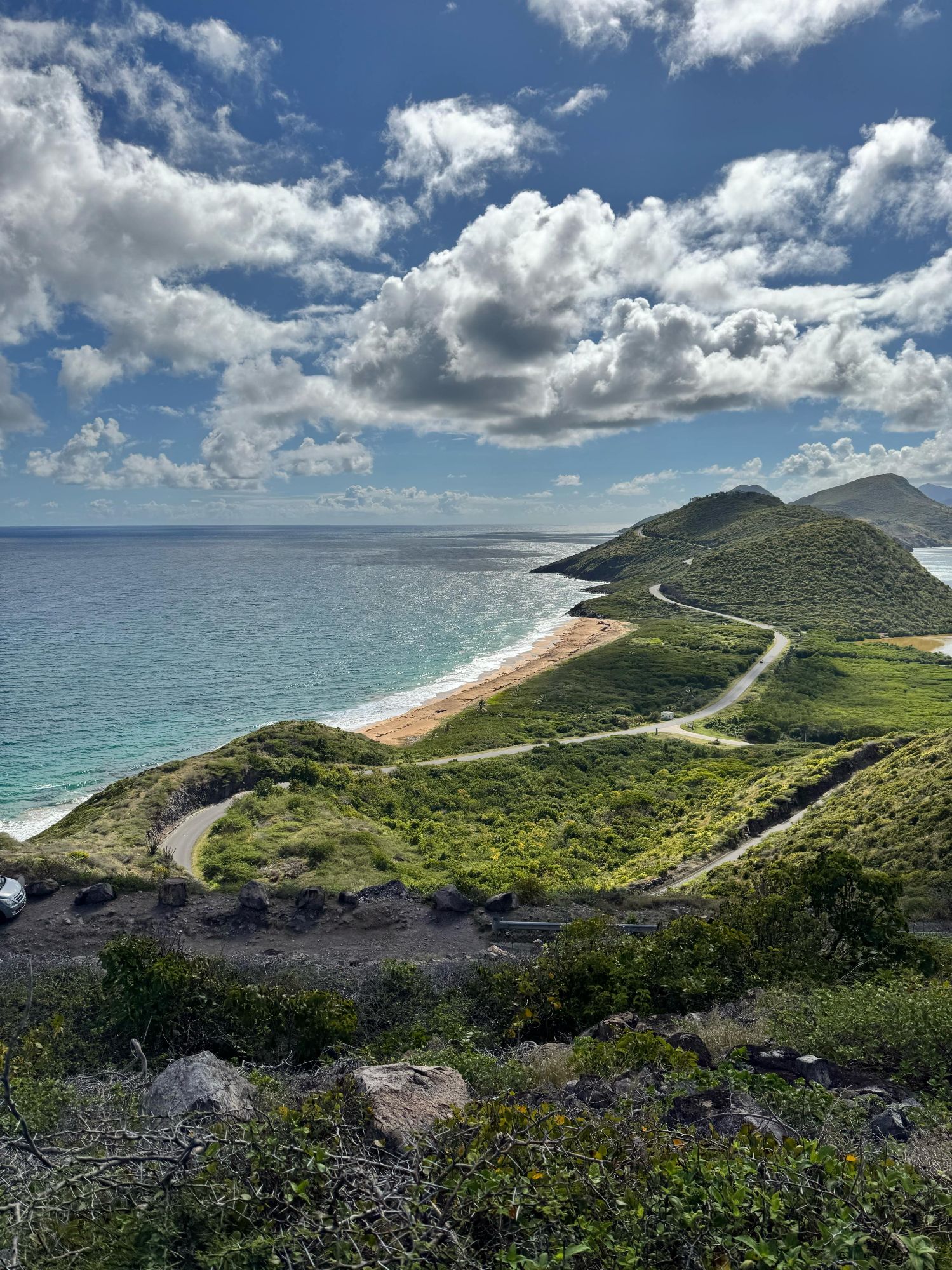 A sweeping aerial view of St. Kitts' Southeast Peninsula with a winding road hugging lush green hills above a turquoise sea.