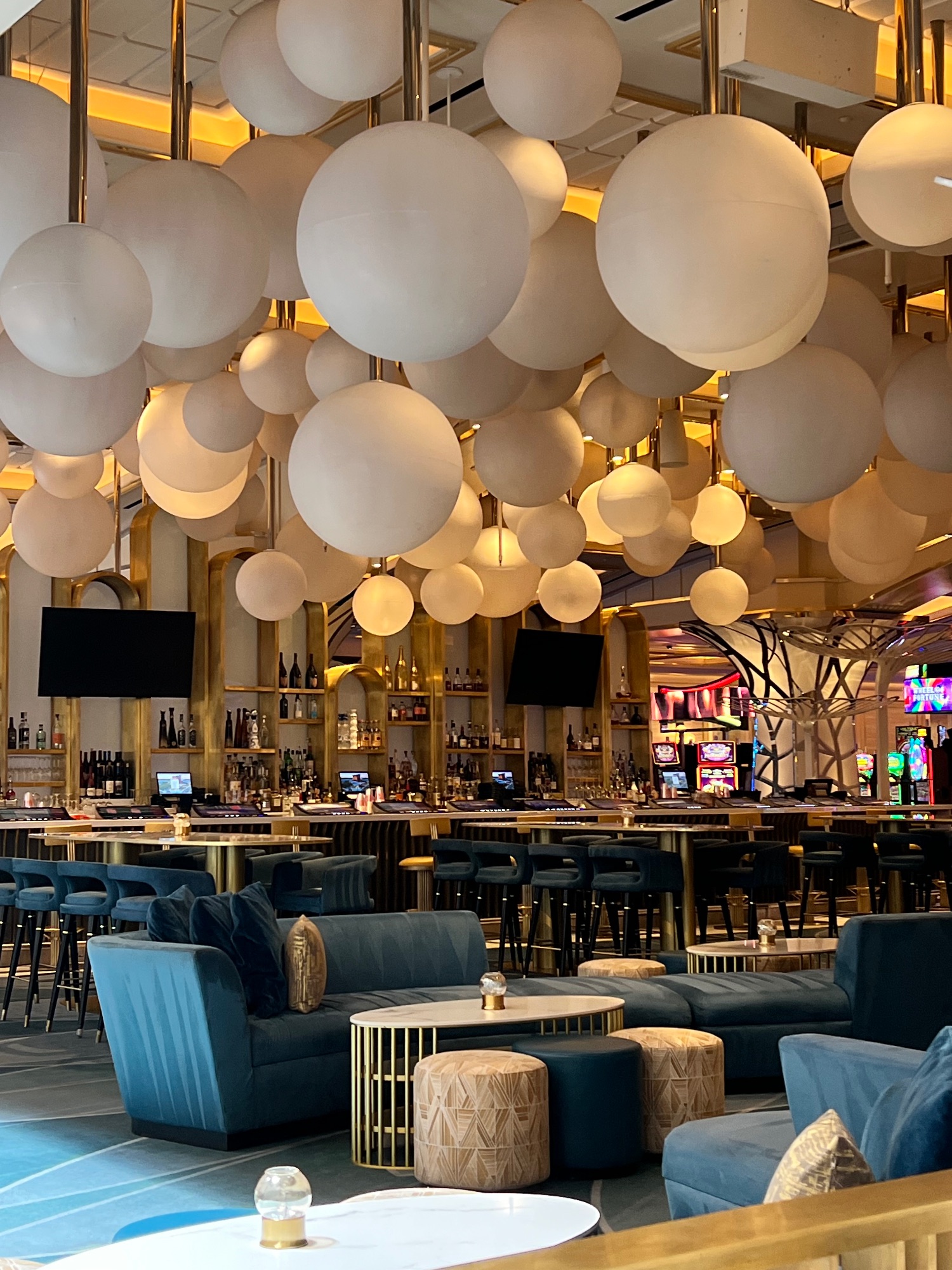 Modern lounge area with suspended frosted glass sphere lights and blue seating beneath gold-accented ceiling