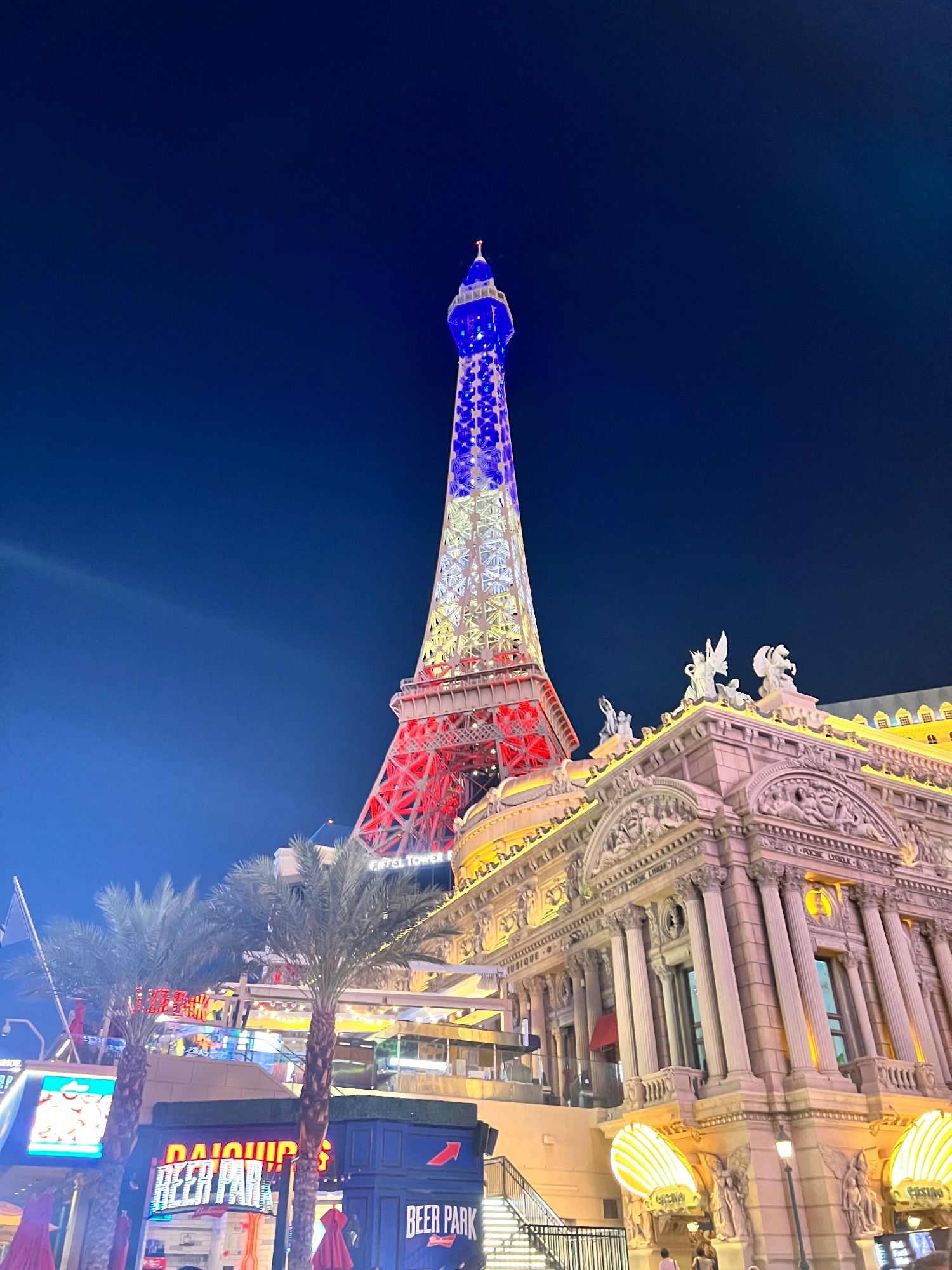 Illuminated replica Eiffel Tower in red and blue lights next to ornate pink building at night in Las Vegas