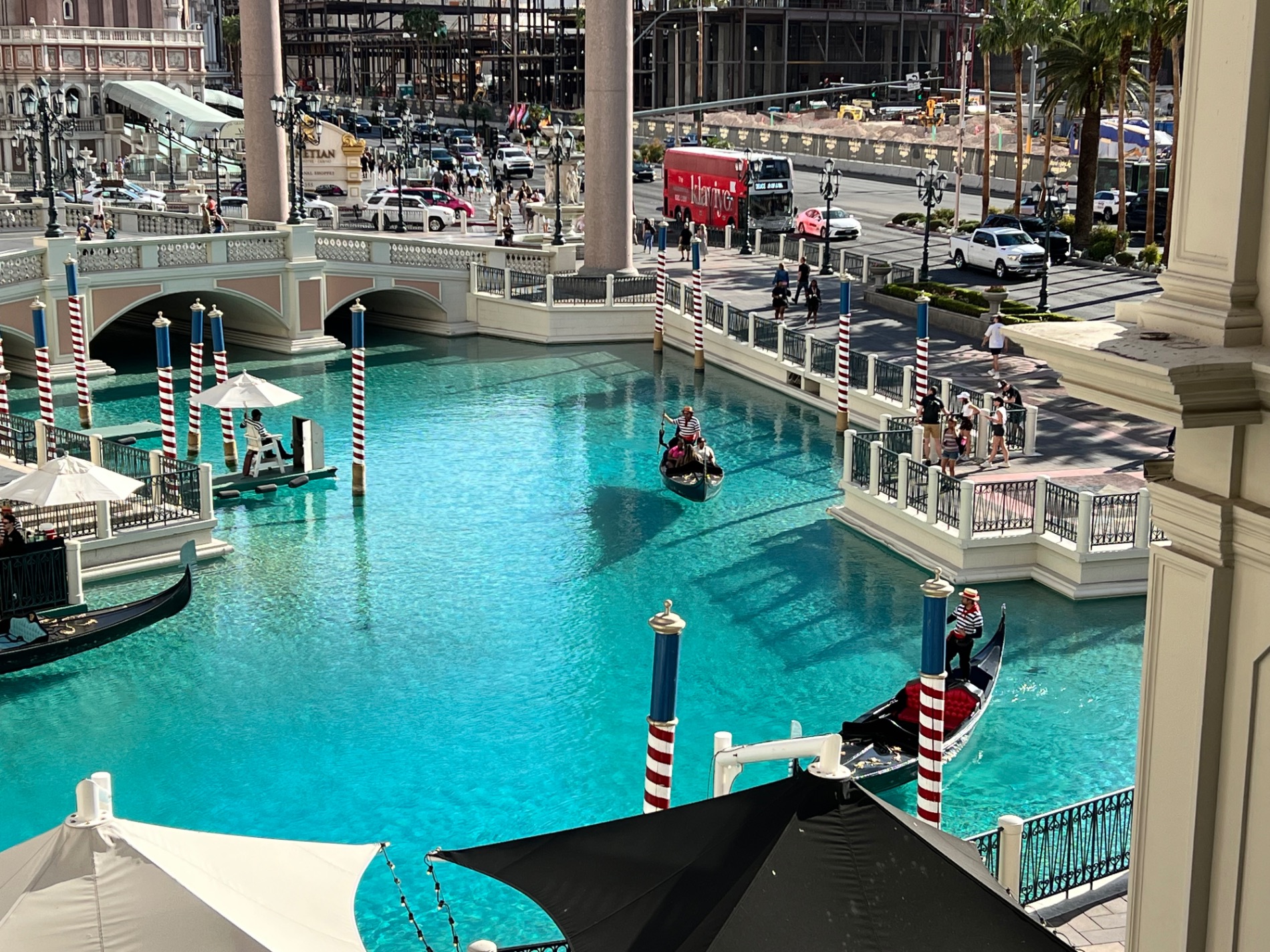Indoor canal with turquoise water, gondolas, striped mooring poles and Venetian-style arched bridges
