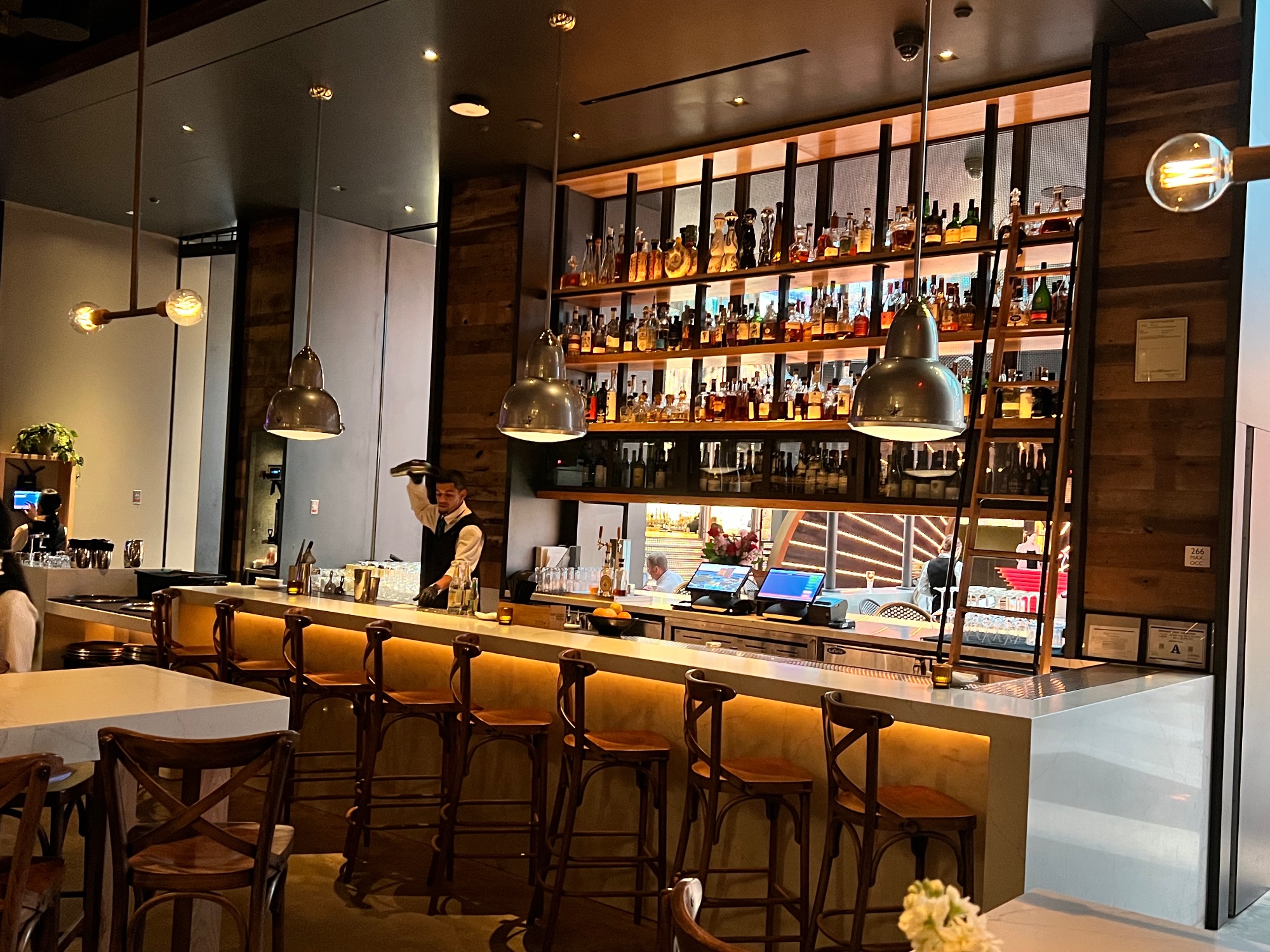 Modern bar interior with wood shelving displaying liquor bottles, pendant lights and wooden bar seating