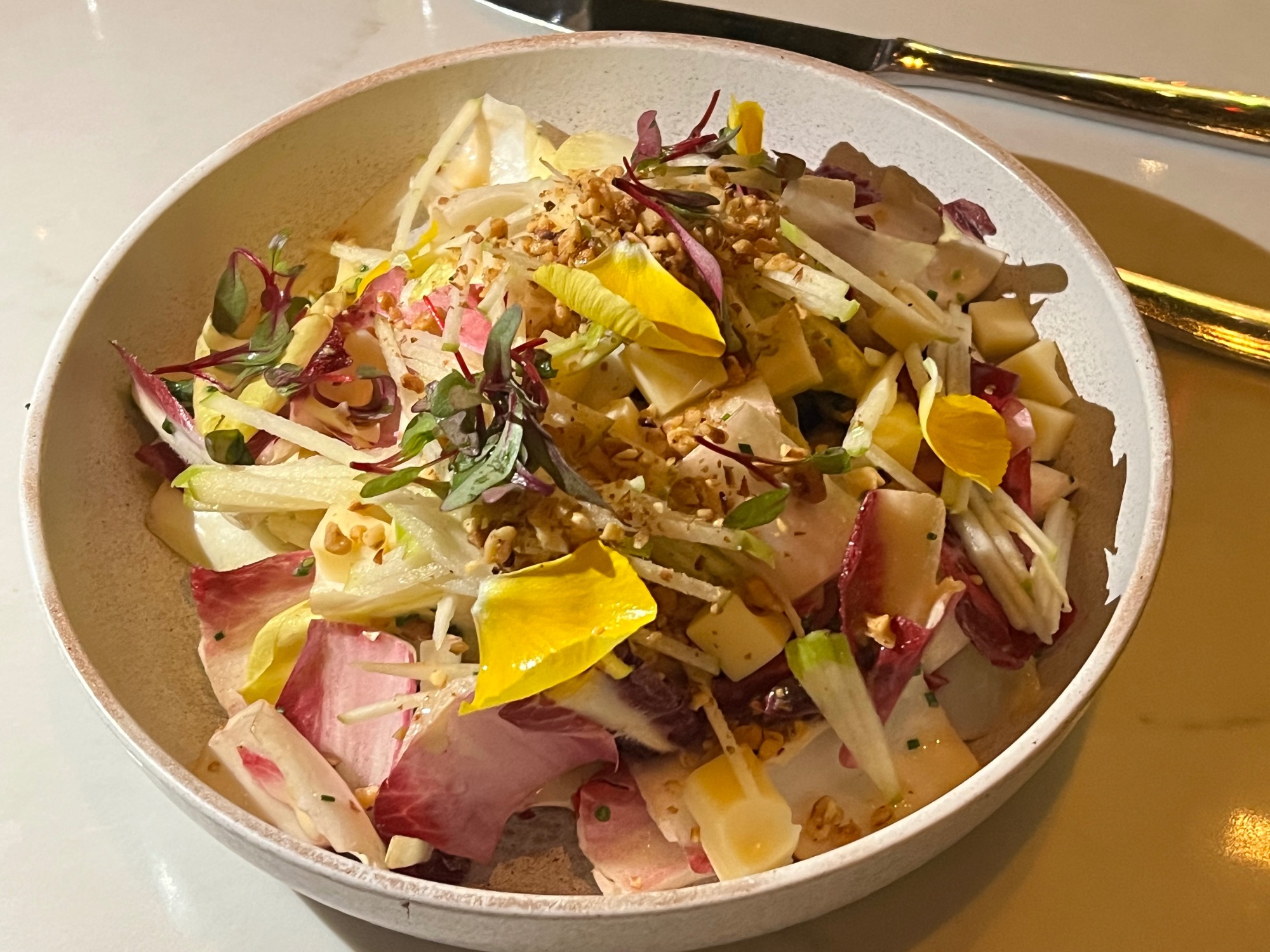 Artfully plated salad with colorful edible flowers, greens and microgreens on white plate