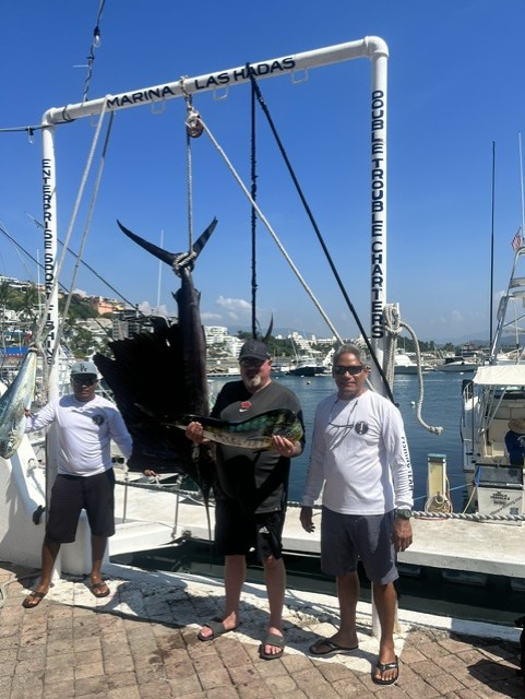Two men pose with a large black marlin hanging from a marina scale at Marina Las Hadas