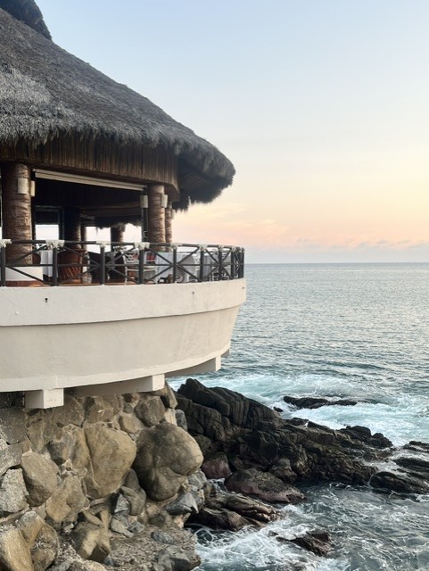 Thatched-roof beachfront palapa overlooks rocky coastline and calm ocean at sunset in Manzanillo