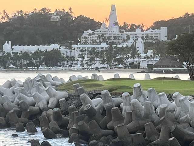 Concrete wave breakers line the shore with white beachfront resort and church spire at sunrise