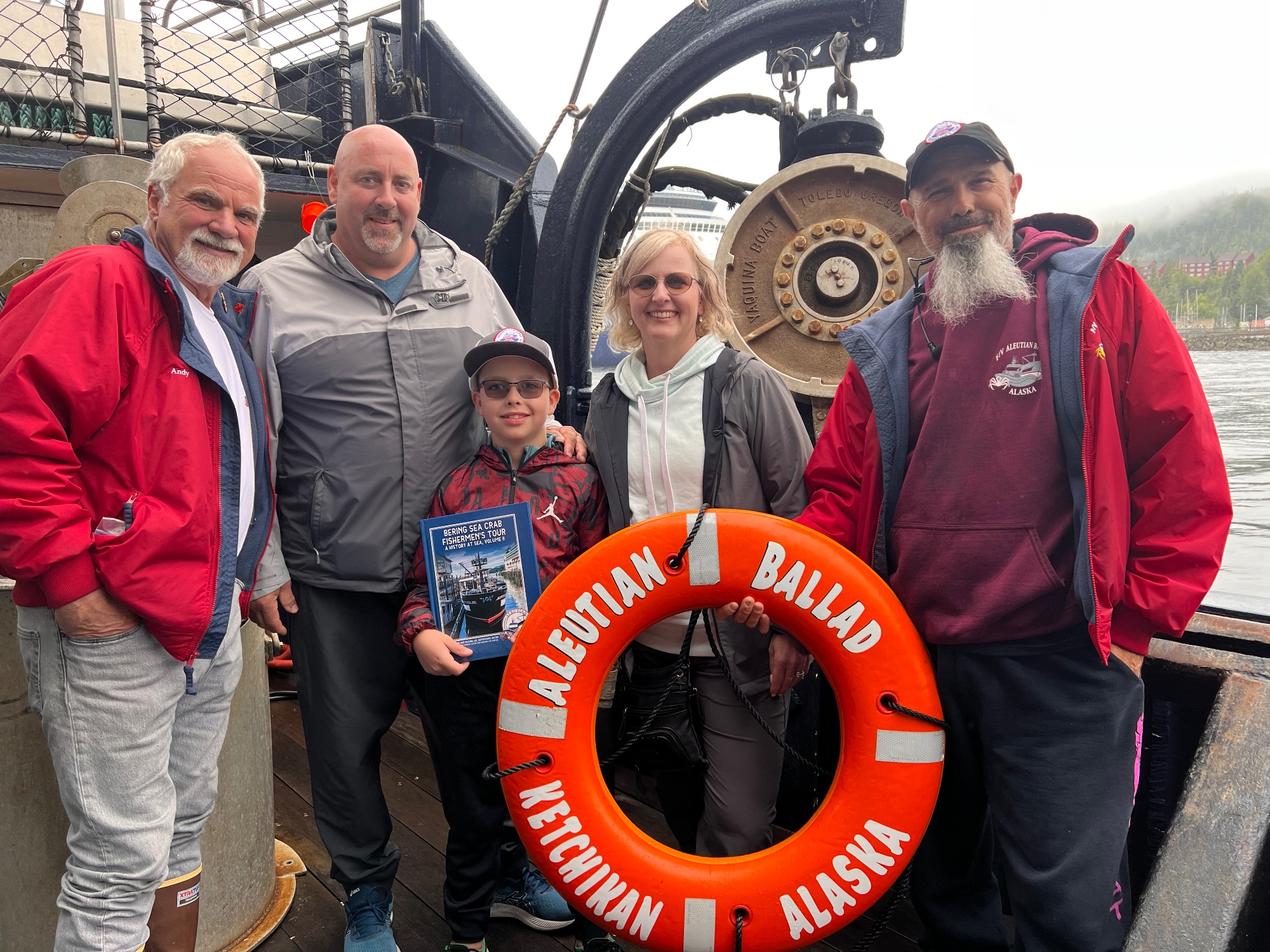 Family of five posing on fishing boat with life ring labeled Alaskan Ballad