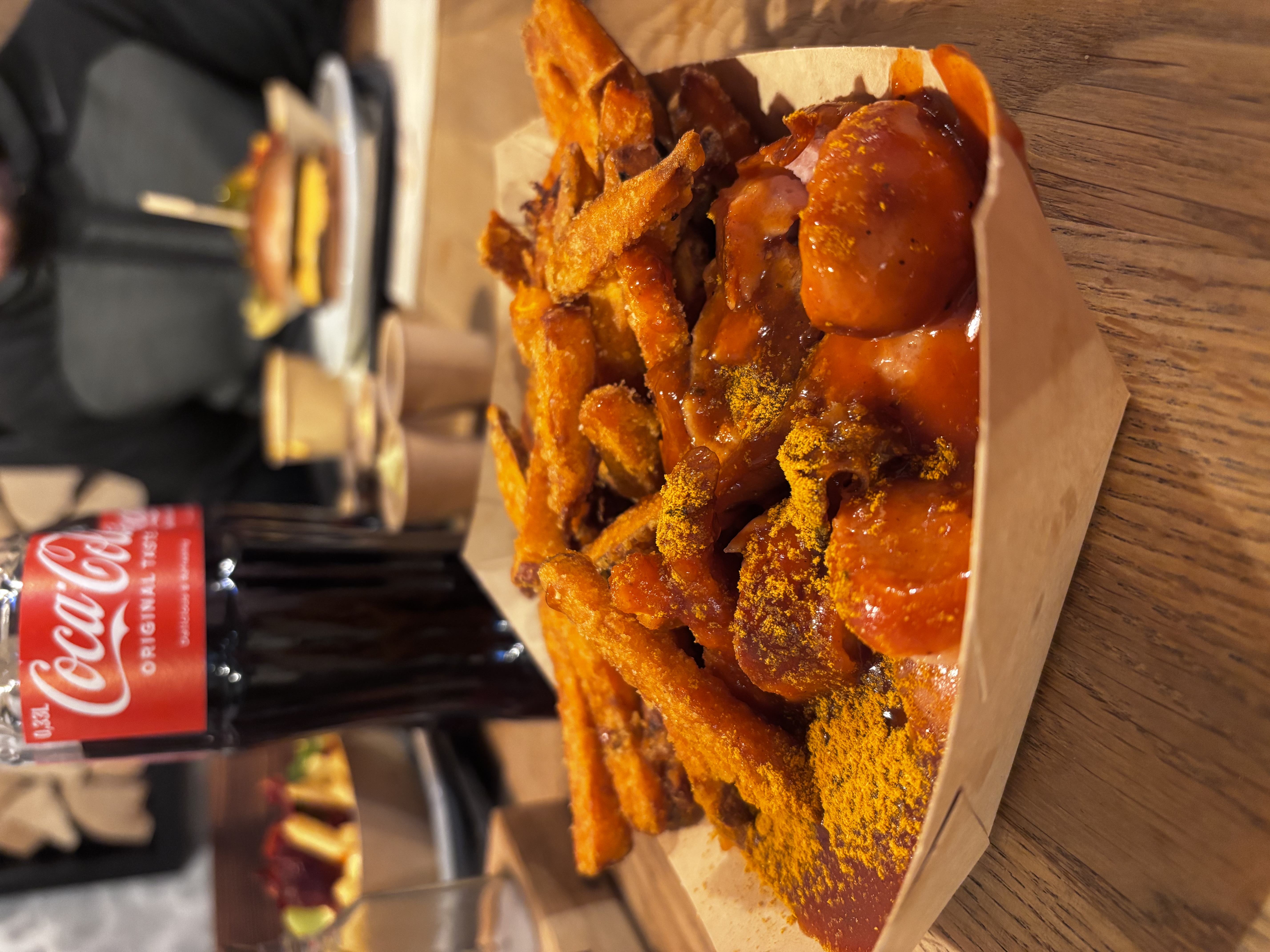 Spiced curry fries and meatballs on a wooden plate with Coca-Cola bottle