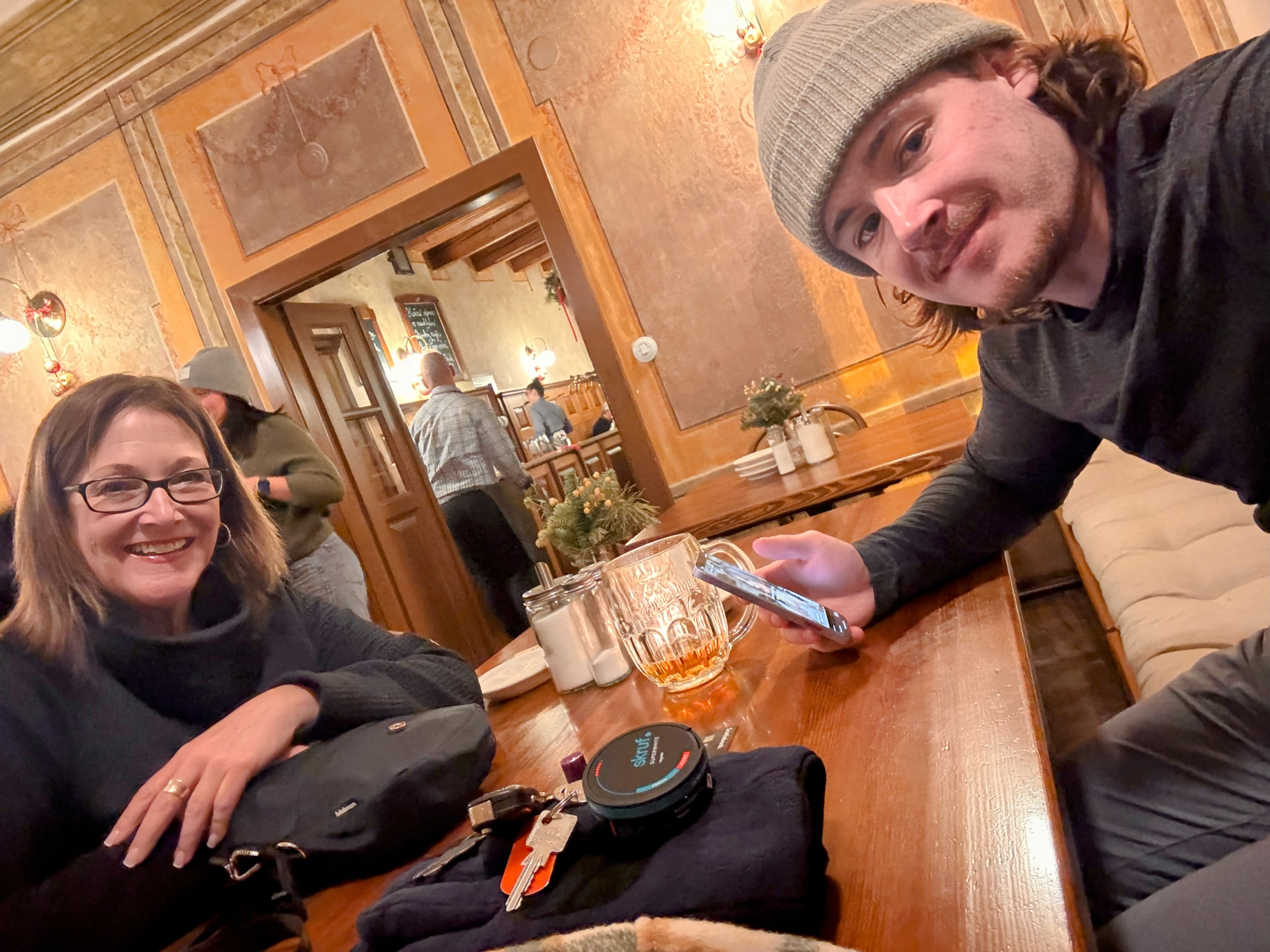 Two people at a bar counter with drinks and snacks in a warm wooden interior