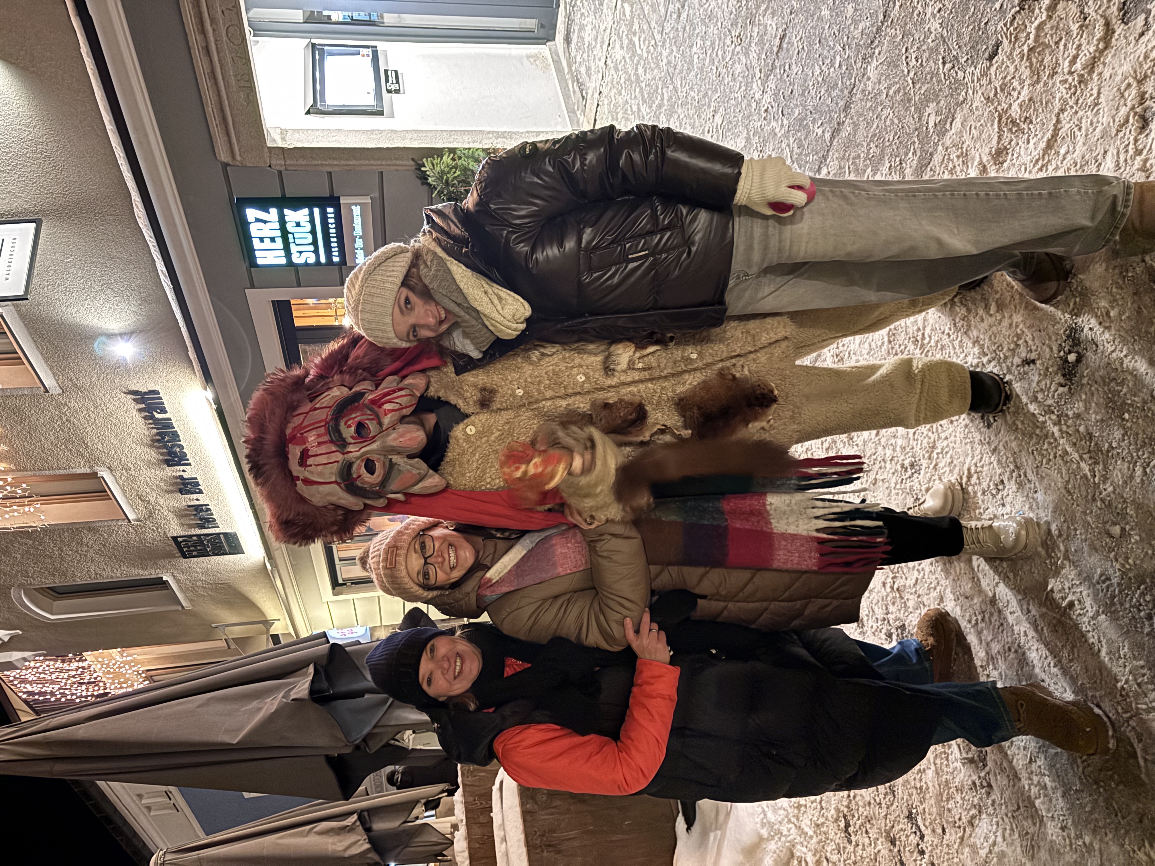 Group of people posing with a costumed krampus character on a snowy street at night