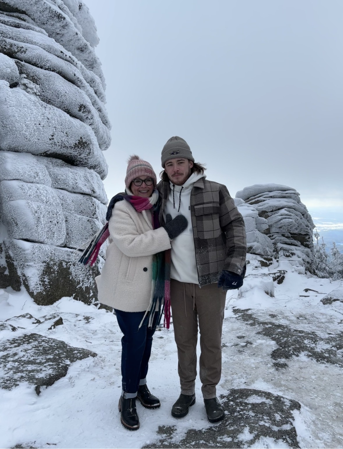 Couple standing between large snow-covered rock formations in a winter forest