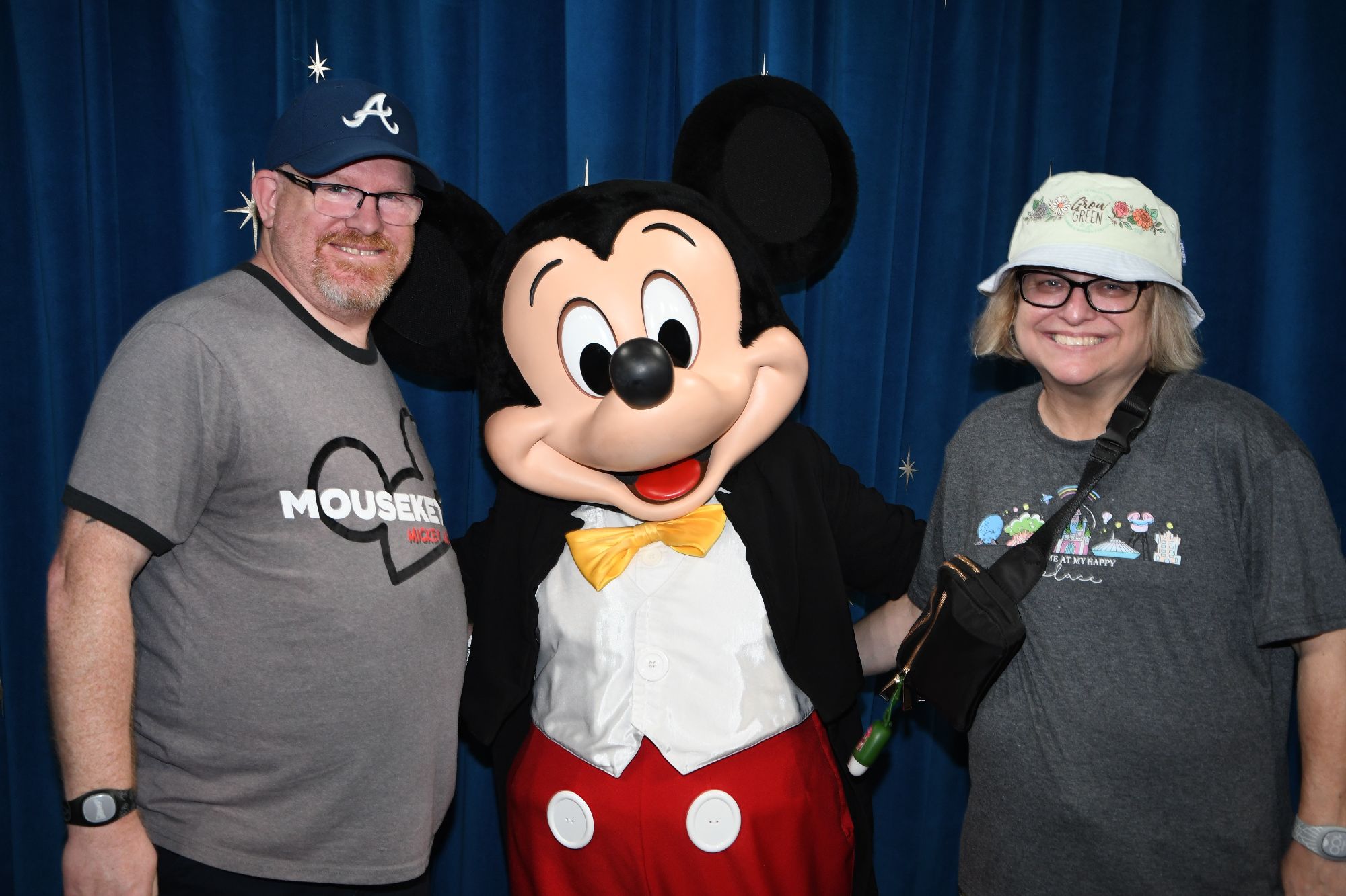 A man and woman pose with Mickey Mouse character in front of a blue curtain backdrop at Walt Disney World
