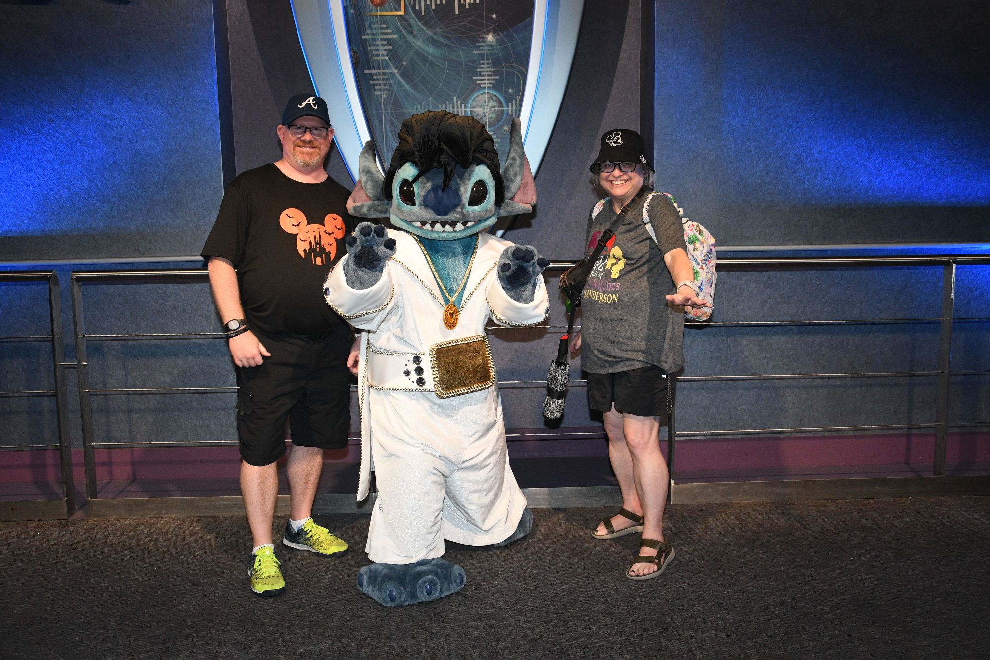 A man and woman pose with an Imagineer character in white costume at what appears to be a Disney World attraction or pavilion